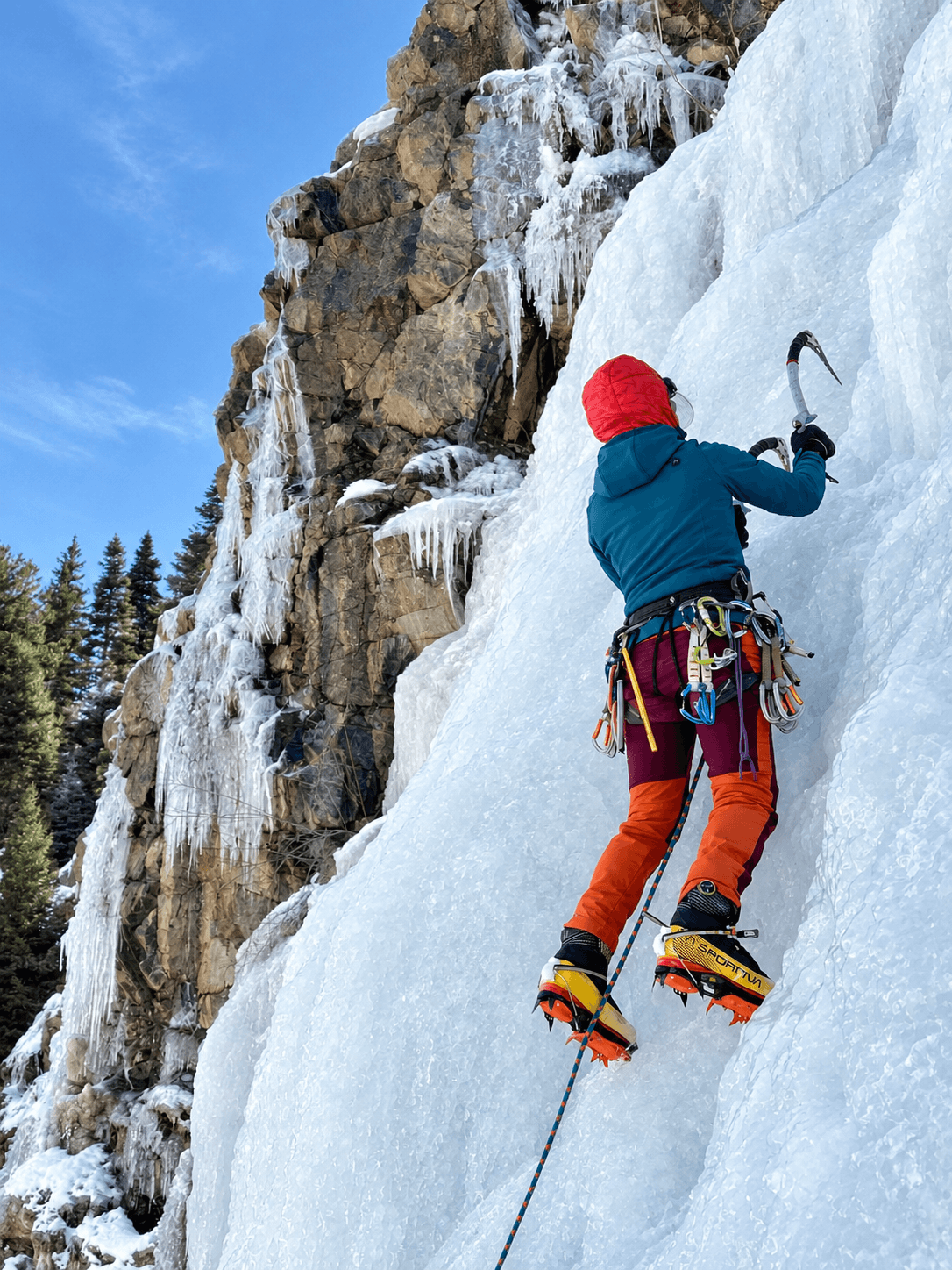 A climber in red pants and blue jacket practices leading an ice climbing route in the Ouray Ice Park.