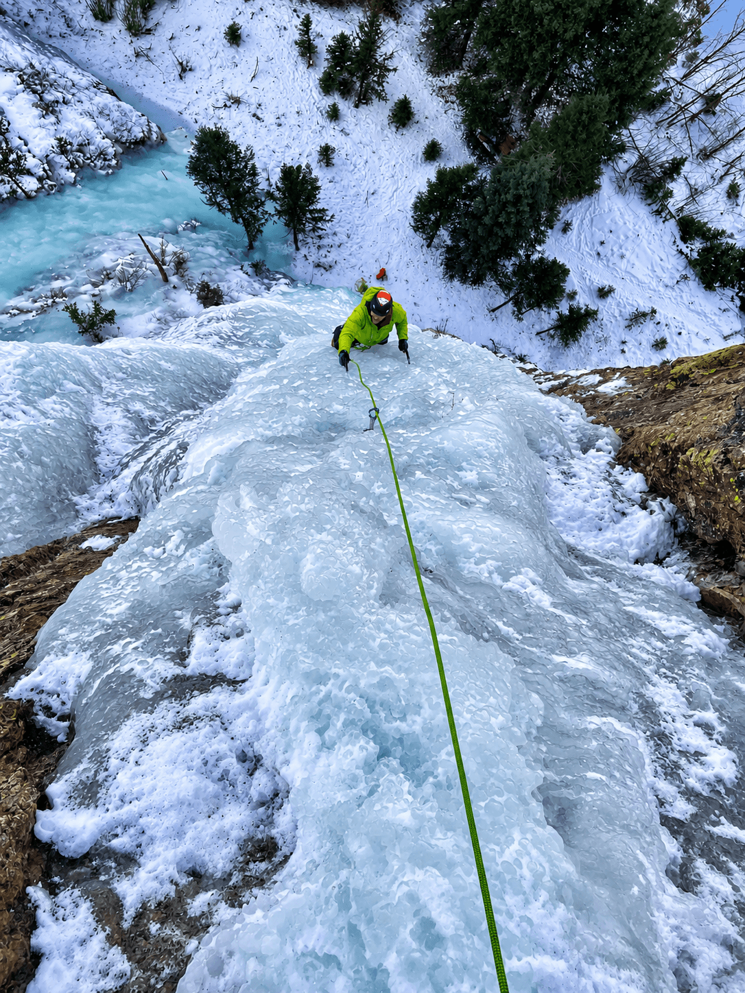 A person in a green jacket is ice climbing a steep route of blue ice in Lake City, Colorado.