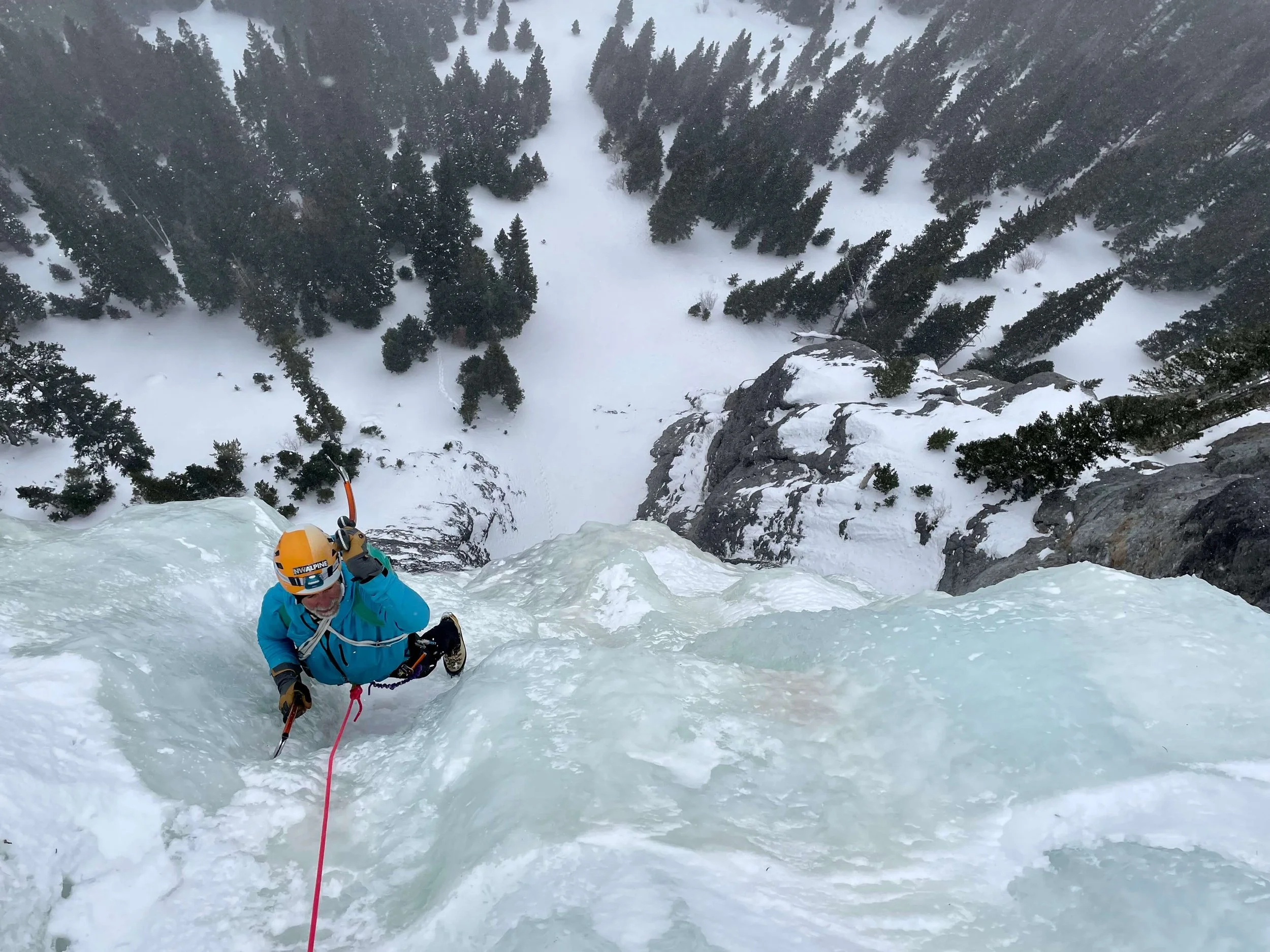 A climber in a blue jacket is ice climbing a steep pitch in Ouray, Colorado.