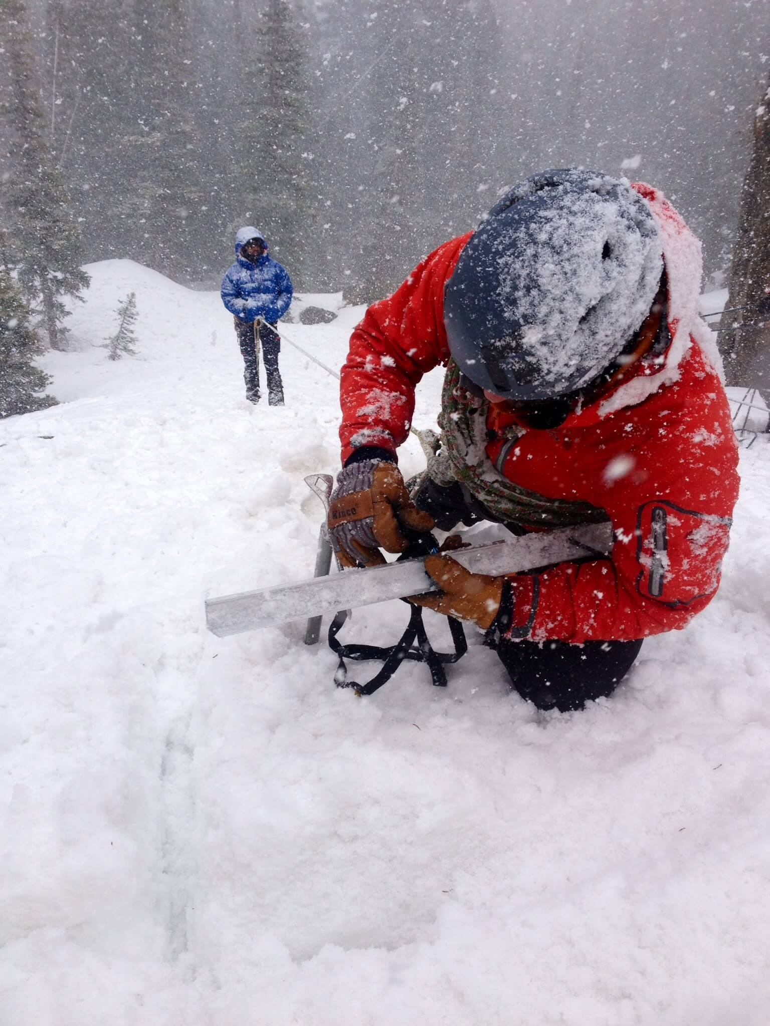 A climber with a red jacket practices crevasse rescue in a snowstorm during an introduction to mountaineering course.