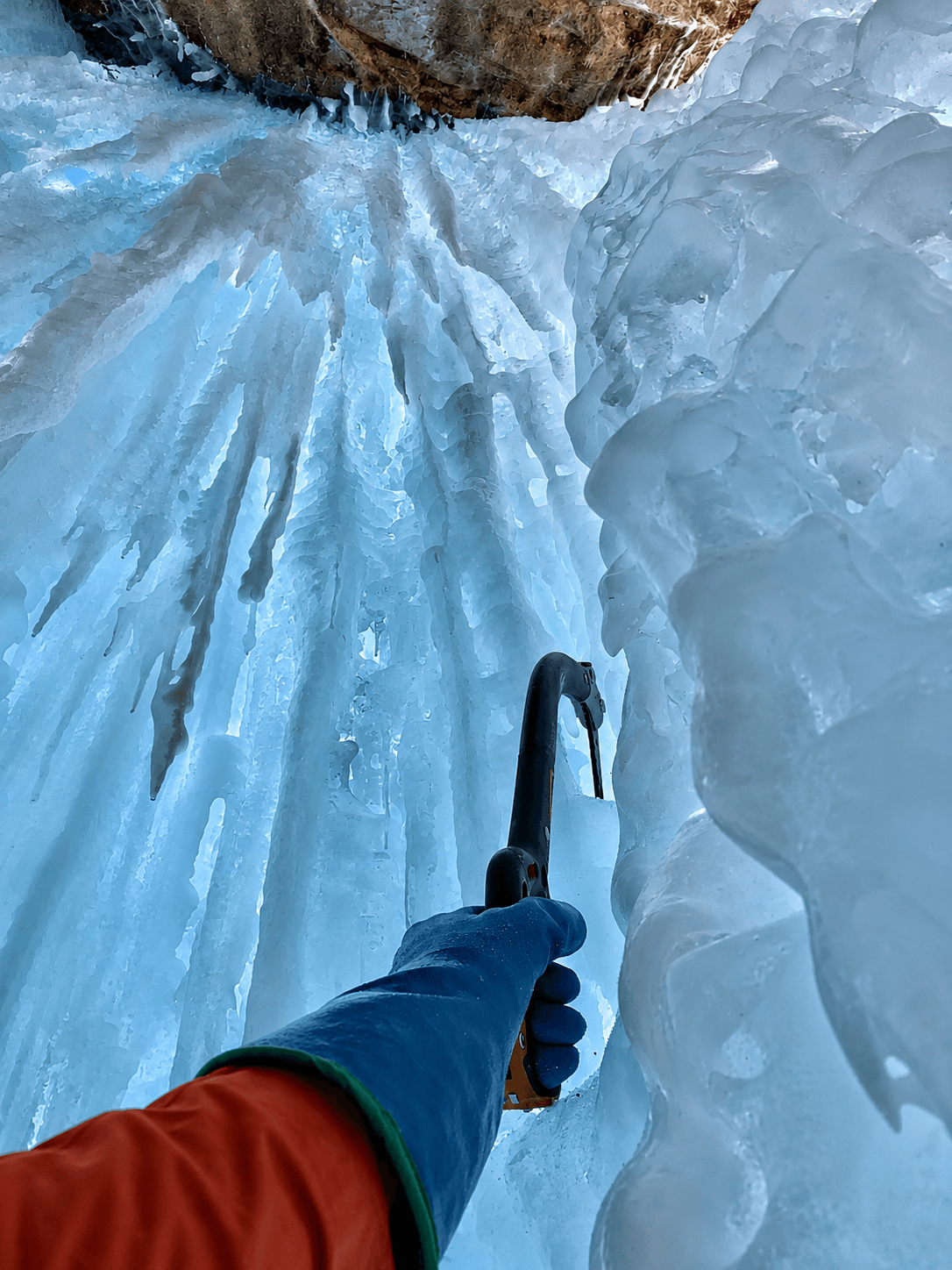 An ice climber is swinging his ice tool into a blue pillar of ice.