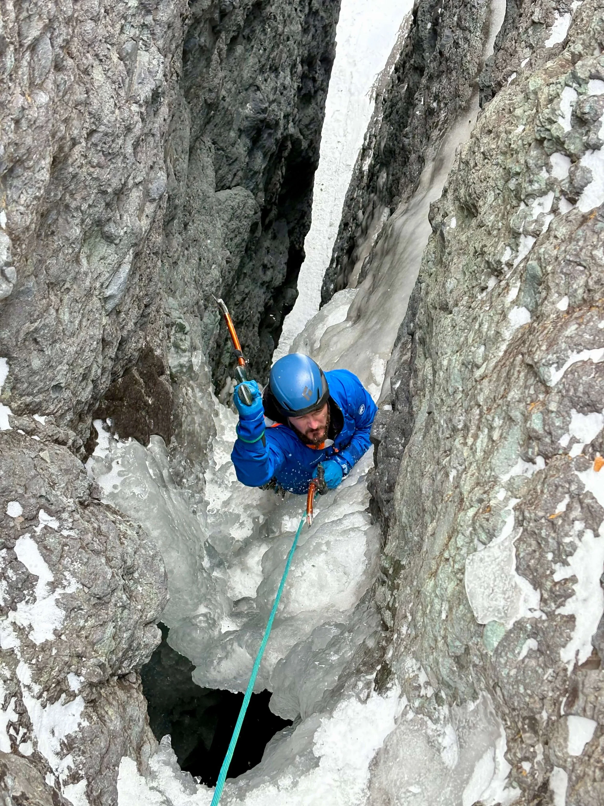 A climber in a blue jacket is swinging his ice tools inside a mixed climbing chimney at the Skylight Area in Ouray.