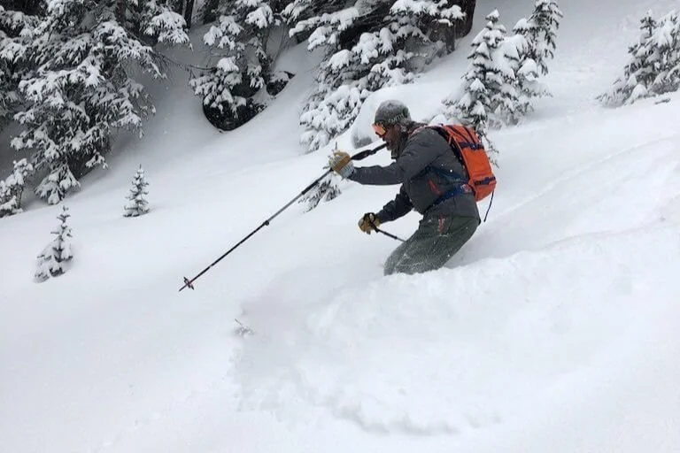 A skier is turning in deep powder, he is getting ready to pole plant as the snow sprays up around him.