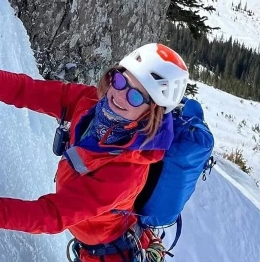 Skyward Mountaineering guide Suzanna Lourie is ice climbing and wearing a red jacket, white helmet and blue backpack.