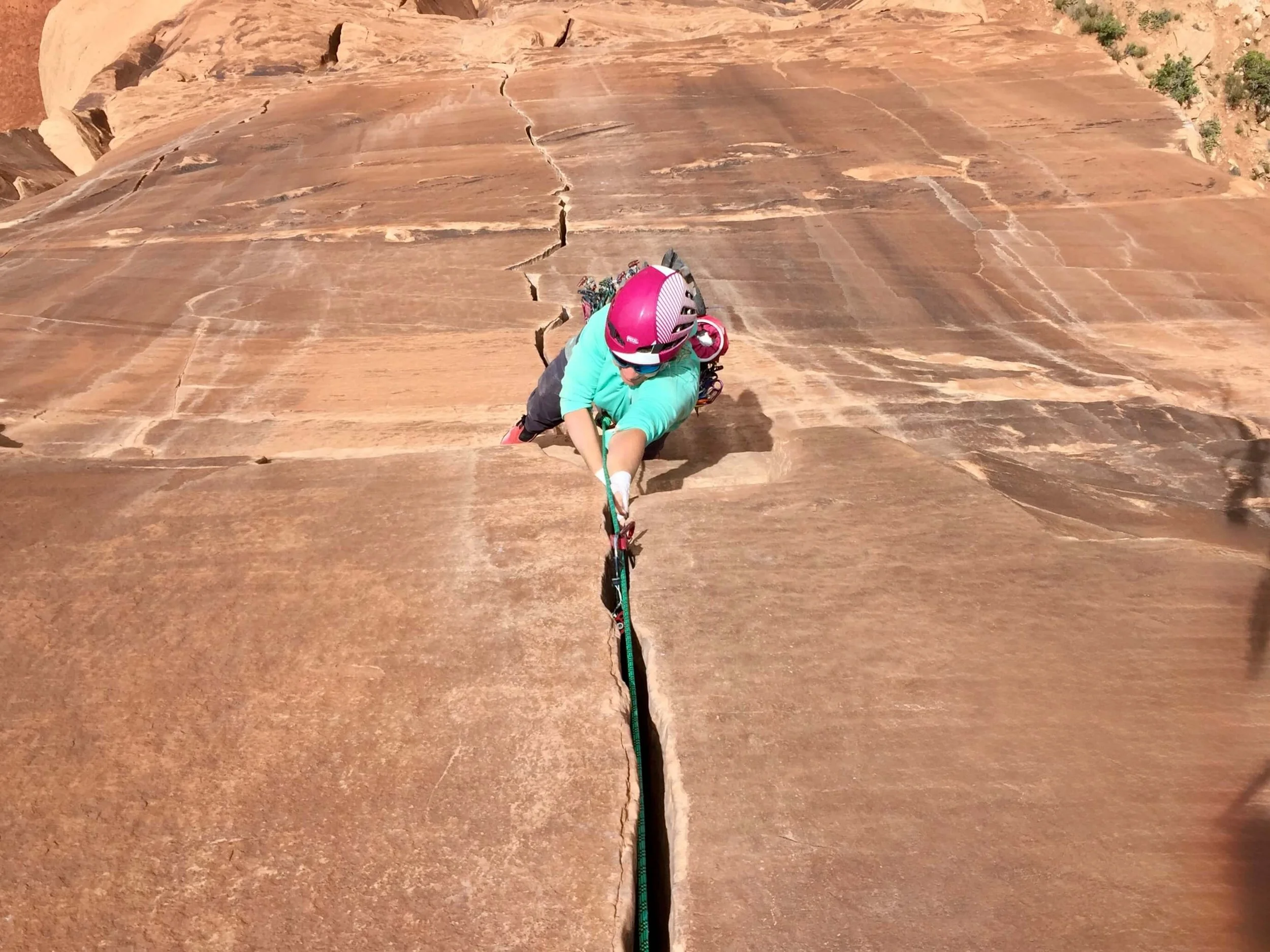 A climber in a blue shirt and pink helmet is crack climbing on the route Medicine Man in Colorado National Monument.