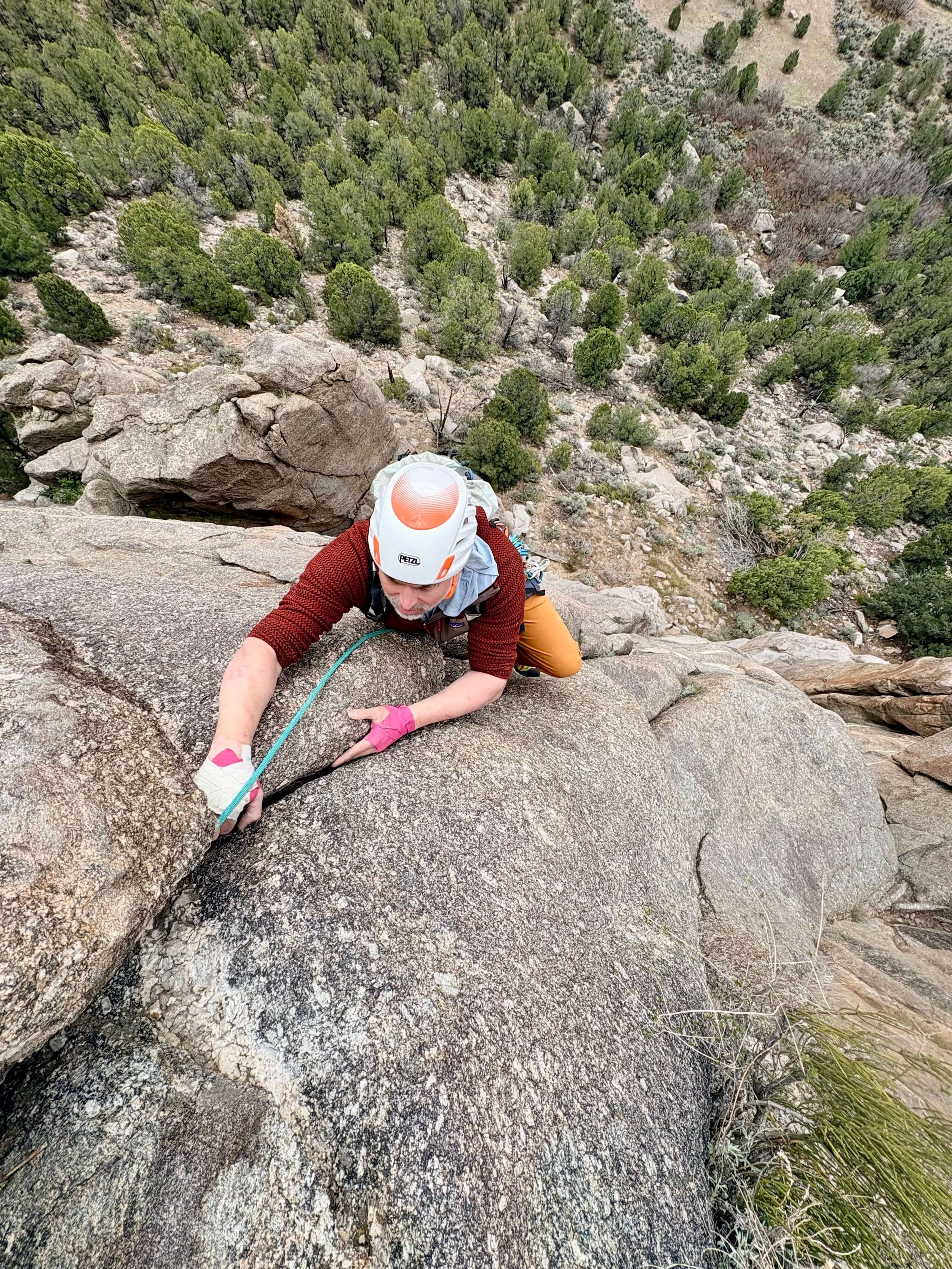 A rock climber in white helmet and red shirt is climbing a crack on Sweet Sunday Serenade in Unaweep Canyon.