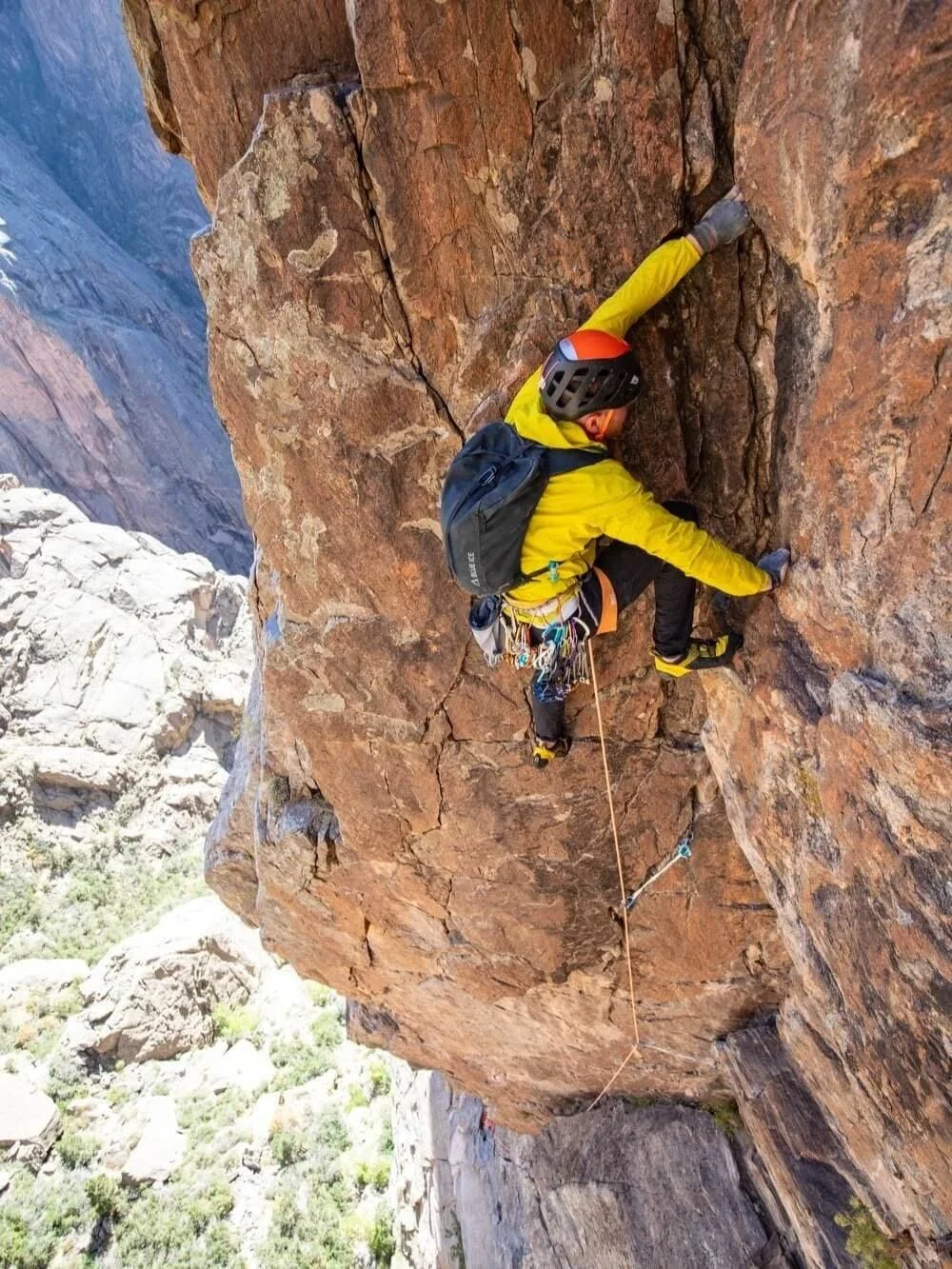 An AMGA Rock Guide in a yellow jacket is leading a rock climbing route in a right facing corner in the Black Canyon.