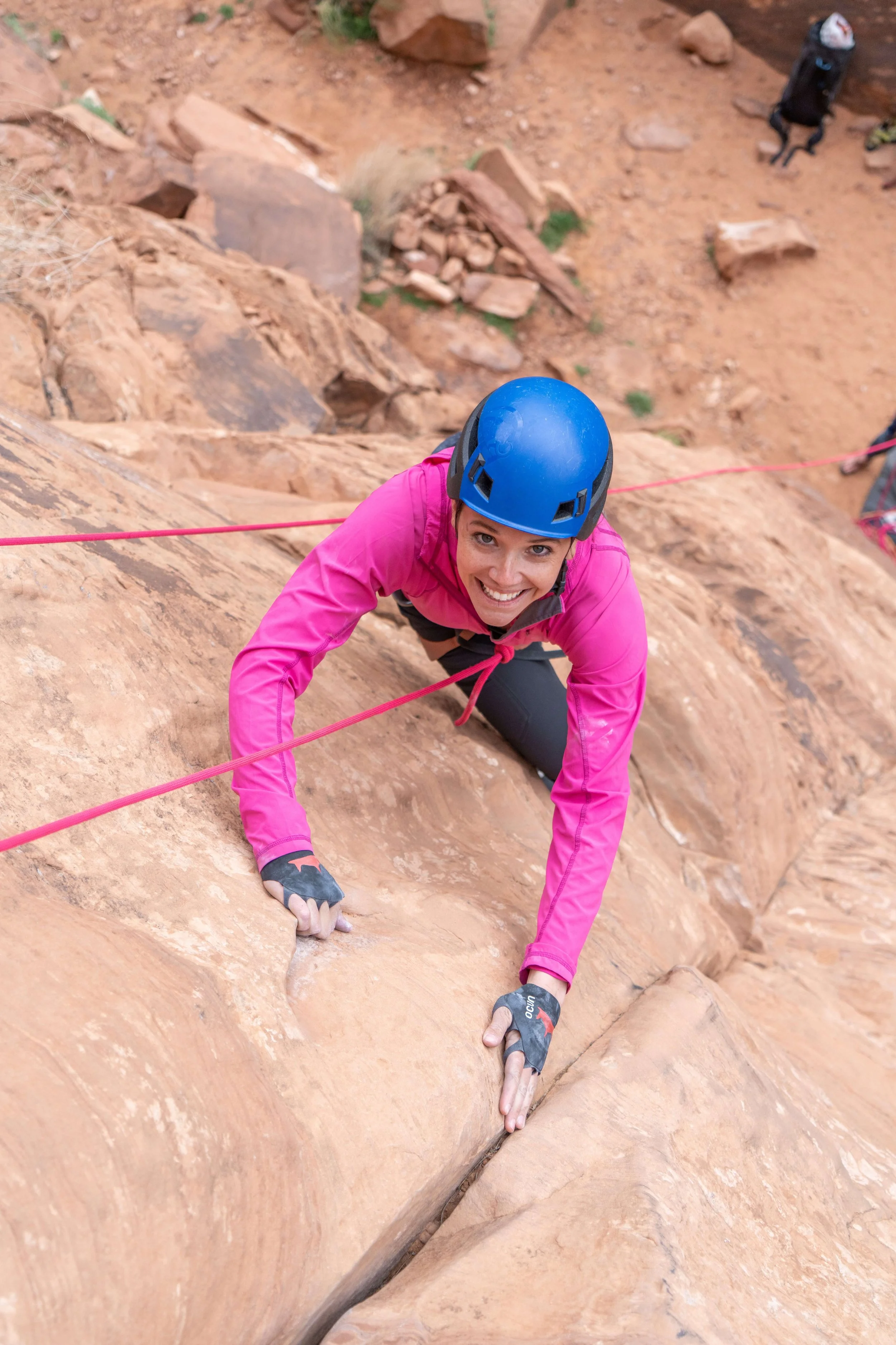 A woman in a blue helmet and pink shirt is climbing at the Ice Cream Parlor on Kane Springs Road in Moab, Utah.