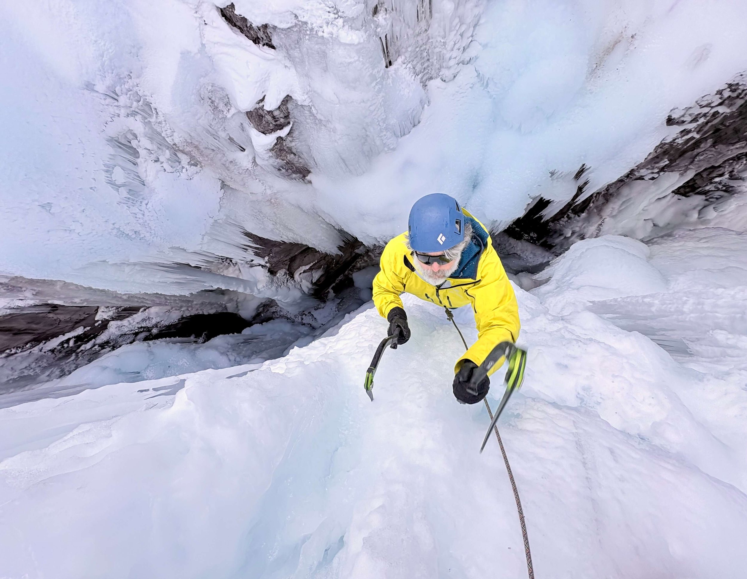 A climber in a yellow jacket is swinging an ice tool on a steep pitch during an ice climbing course in the Ouray Ice Park.