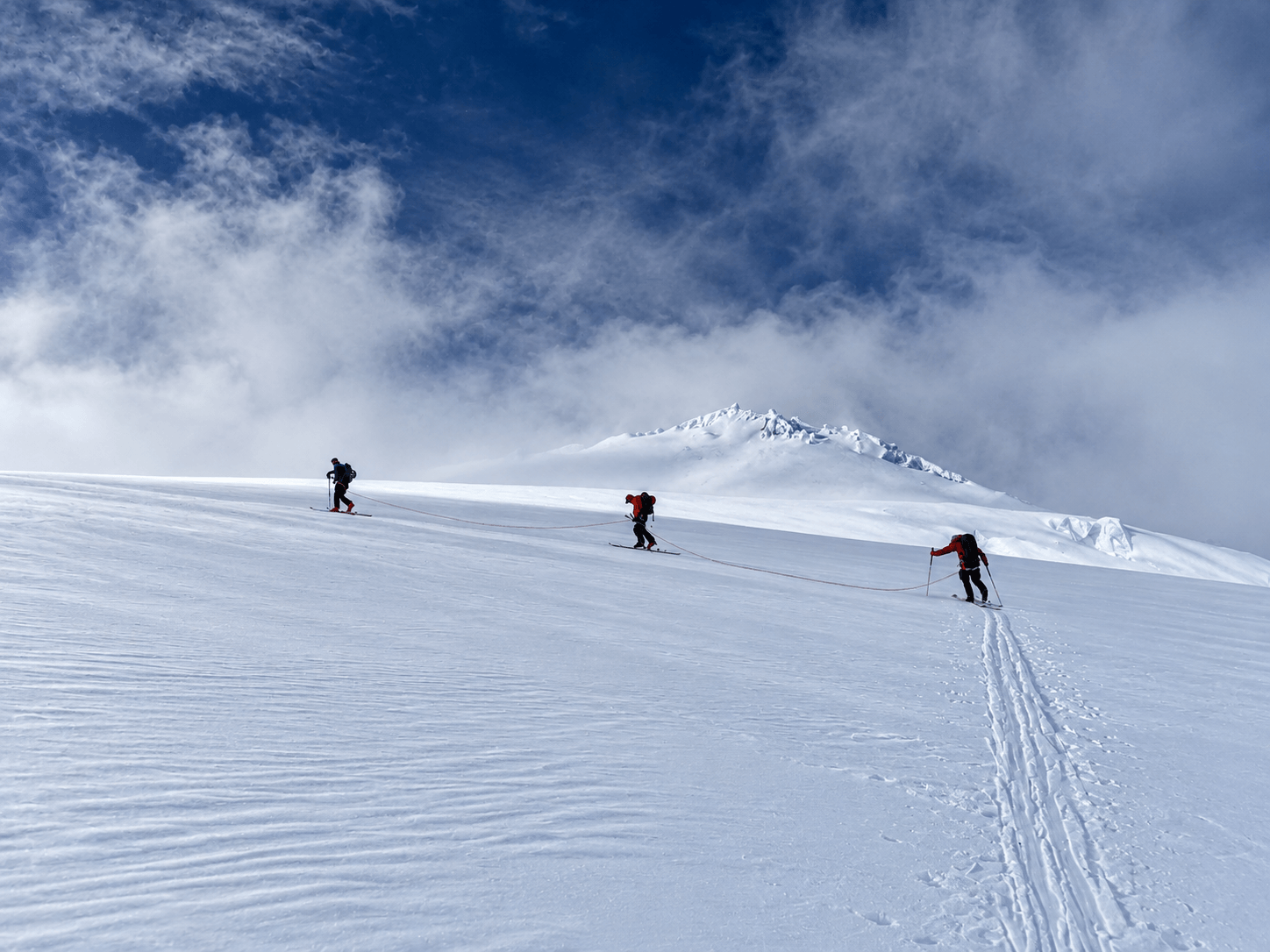 A group of skiers making a switchback turn while climbing a glacier during a ski mountaineering course.
