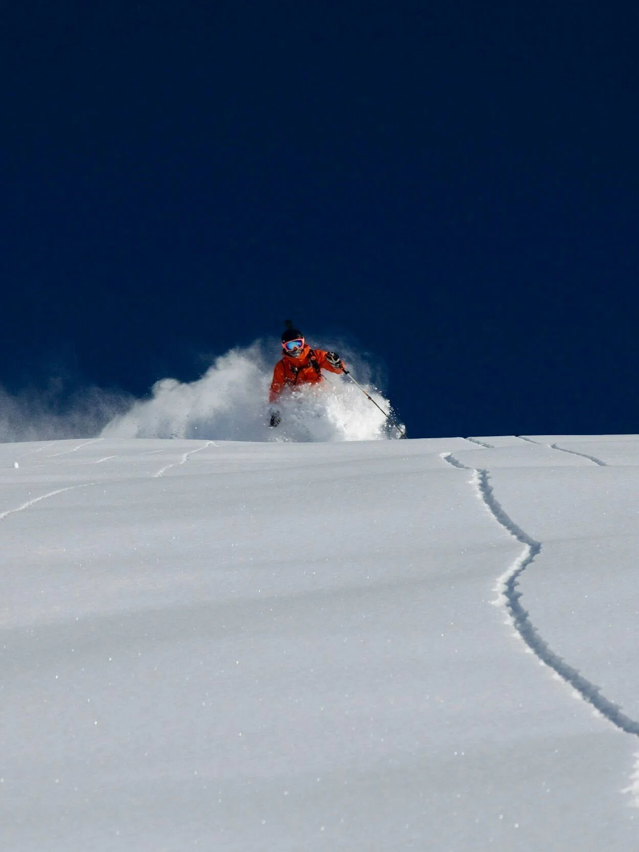 A person skiing down a deep snowy slope on a clear day.
