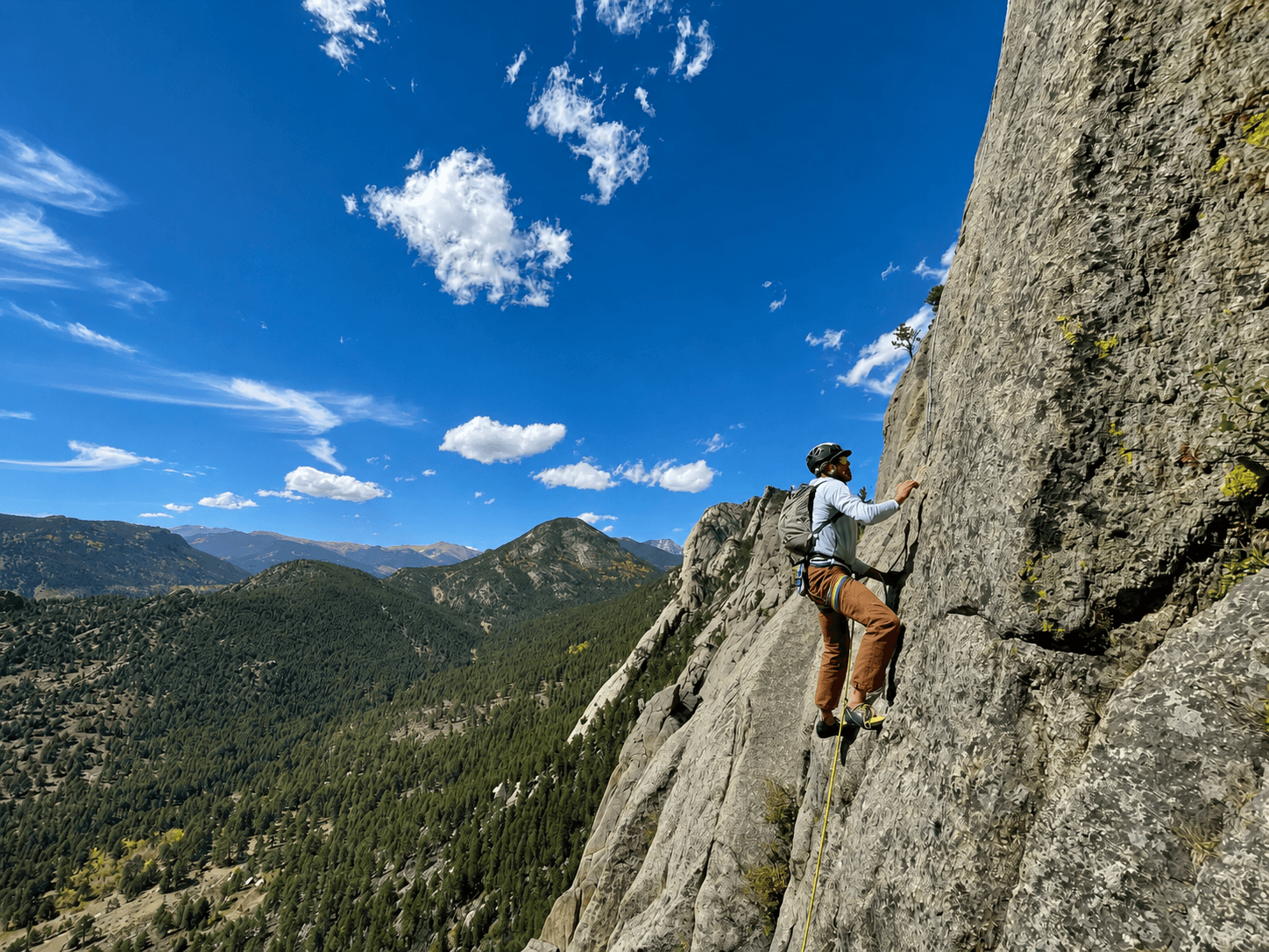 Vince Anderson is climbing a route in Lumpy Ridge with blue skies and mountains in the background.