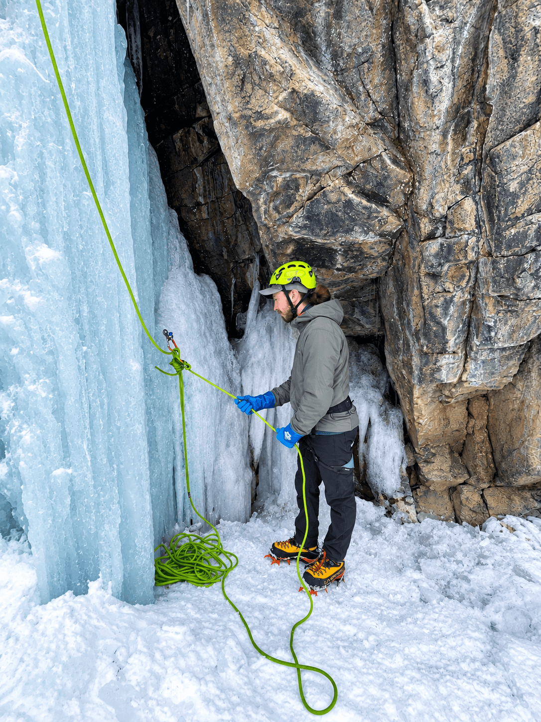 A climber wearing a green helmet is practicing building anchors during an alpine climbing course in the Ouray Ice Park.