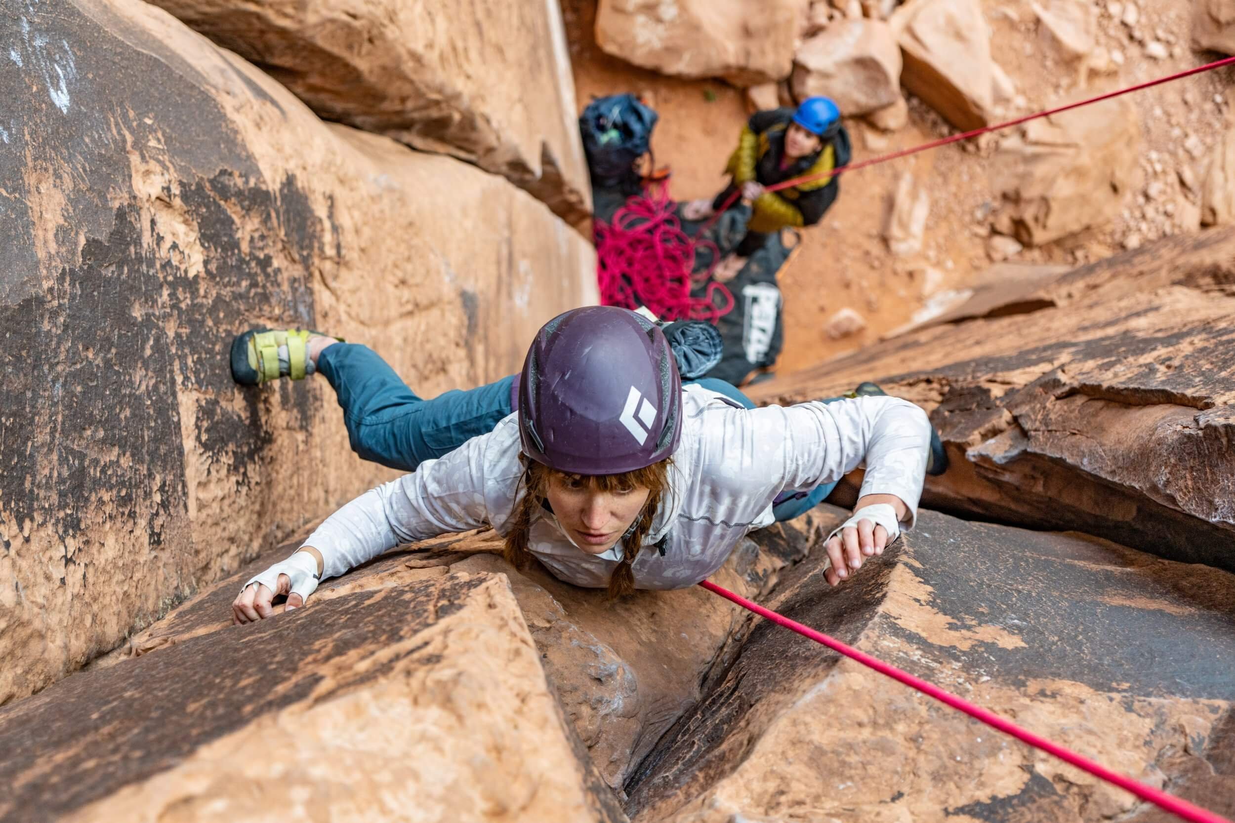A rock climber is top-roping a crack climb in Moab. She is looking up and moving her hand for the next hold above.