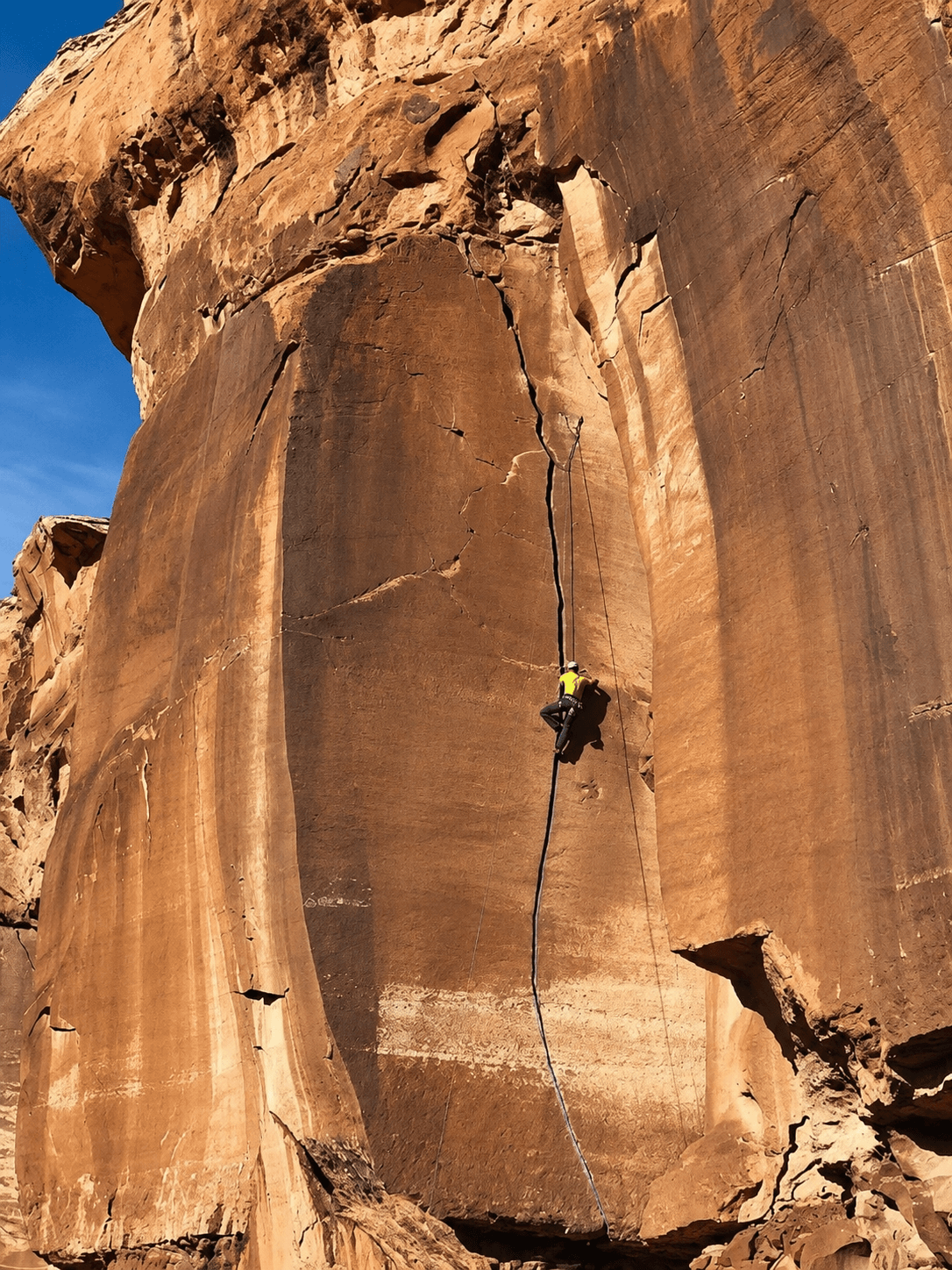 A climber in a yellow shirt is crack climbing at the Cabin Wall in Escalante Canyon.