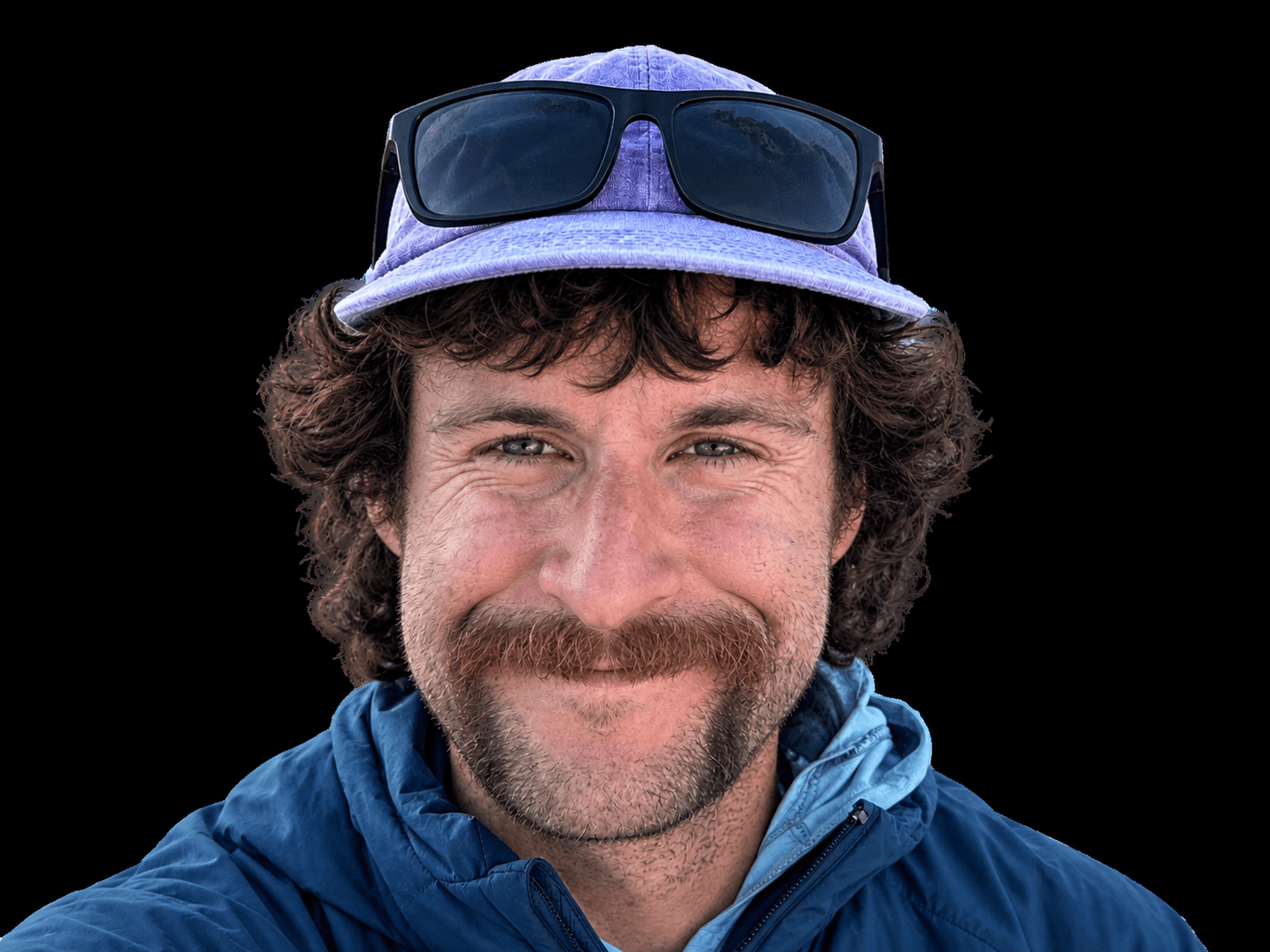 Portrait of Skyward Mountaineering guide, Nik Mirhashemi. He is wearing a purple hat with sunglasses resting on the brim.