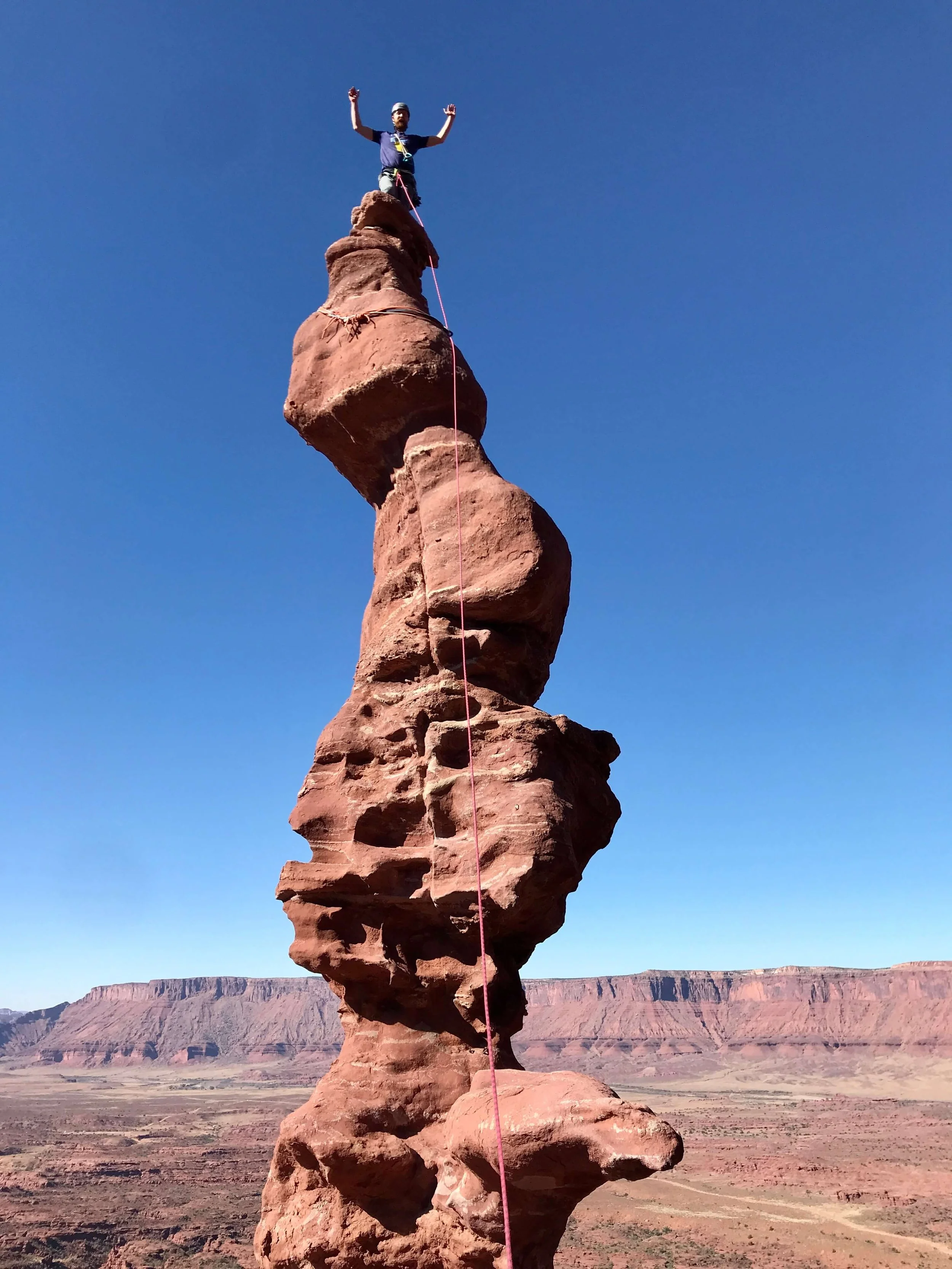 A rock climber is standing on the corkscrew summit of the route, Ancient Art.