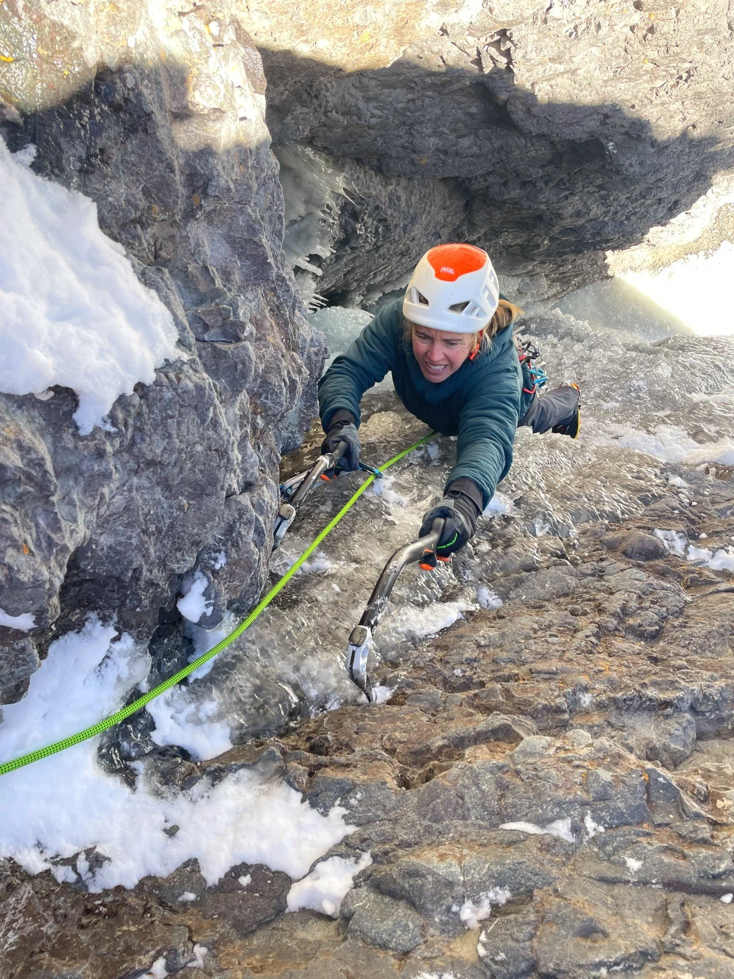 A climber in a green jacket places her ice tool delicately on an edge next to a thin ice smear on the route, Skylight in Ouray, Colorado.