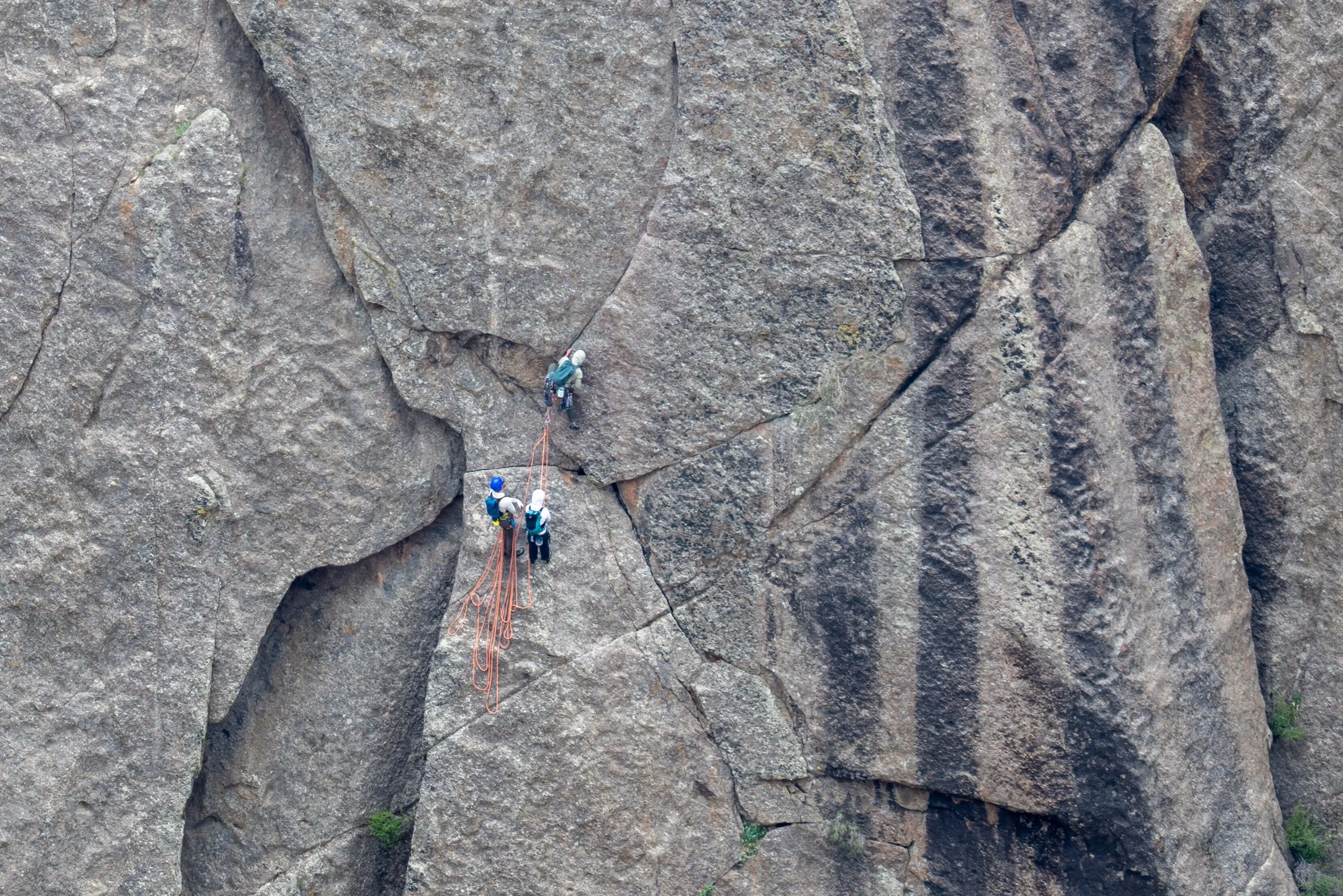 A guide leads up the crux pitch of Comic Relief in the Black Canyon with two climbers below belaying him.