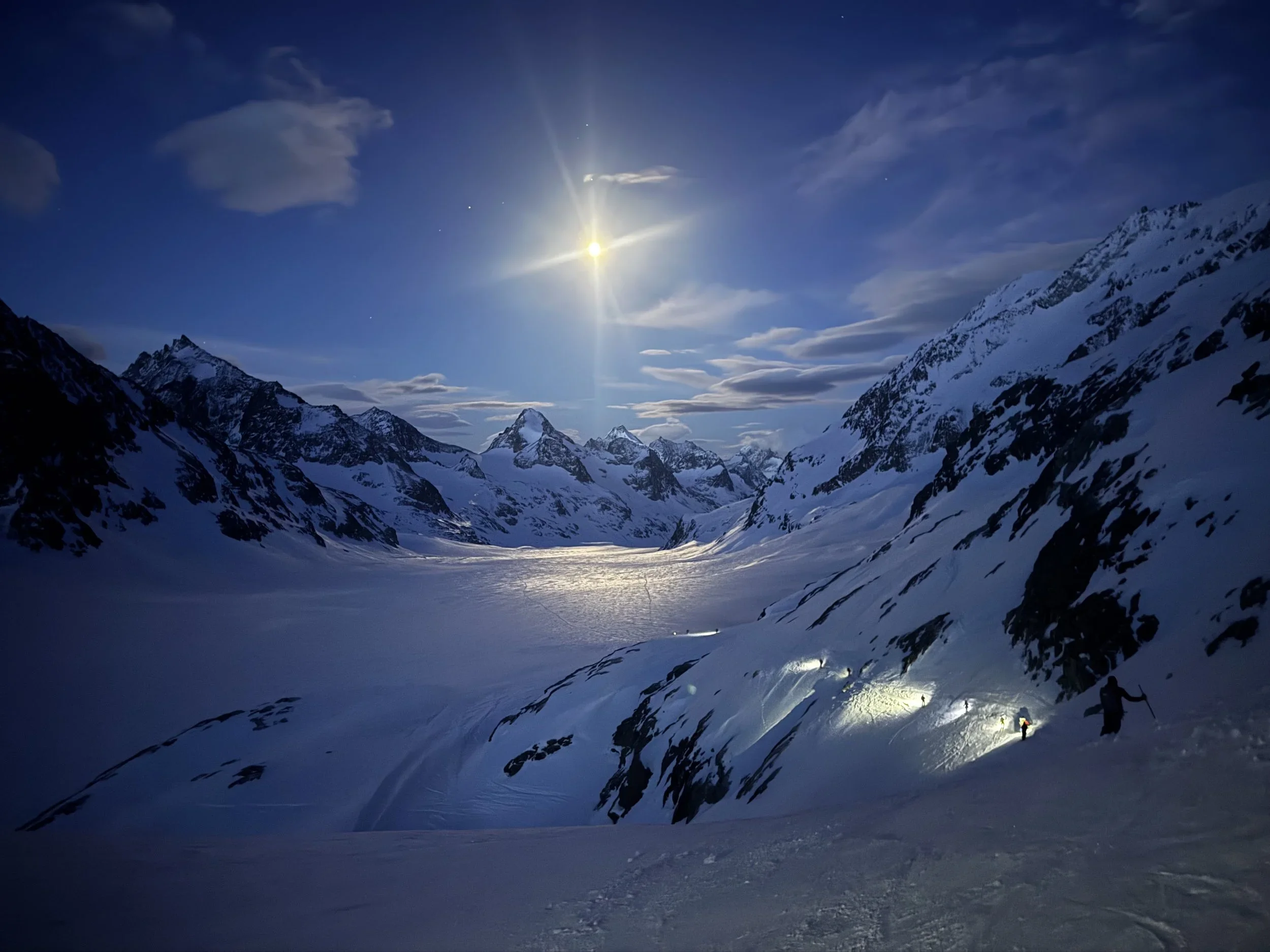 Skiers traverse a glacier during the Haute Route tour with their headlamps casting a glow in front of them.