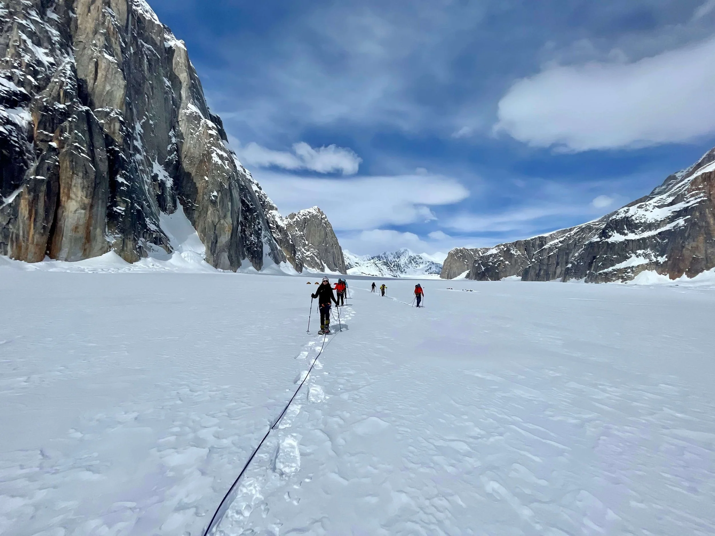 Two rope teams of mountaineers cross the Ruth Gorge glacier with towering peaks, such as Mount Dickey and Barrille behind them.