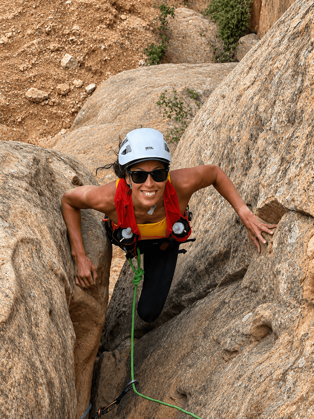 A rock climber in a white helmet and red backpack is climbing on the first pitch of Otto's Route in Colorado National Monument.