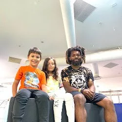 Three children sitting on a bench indoors, smiling and looking at the camera.