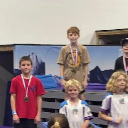 Group of children standing on a podium with medals, celebrating at a ninja event.