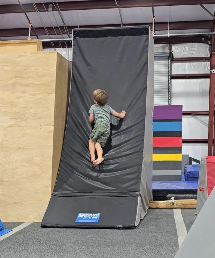 Young boy climbing an indoor padded warp wall at a parkour or ninja park.
