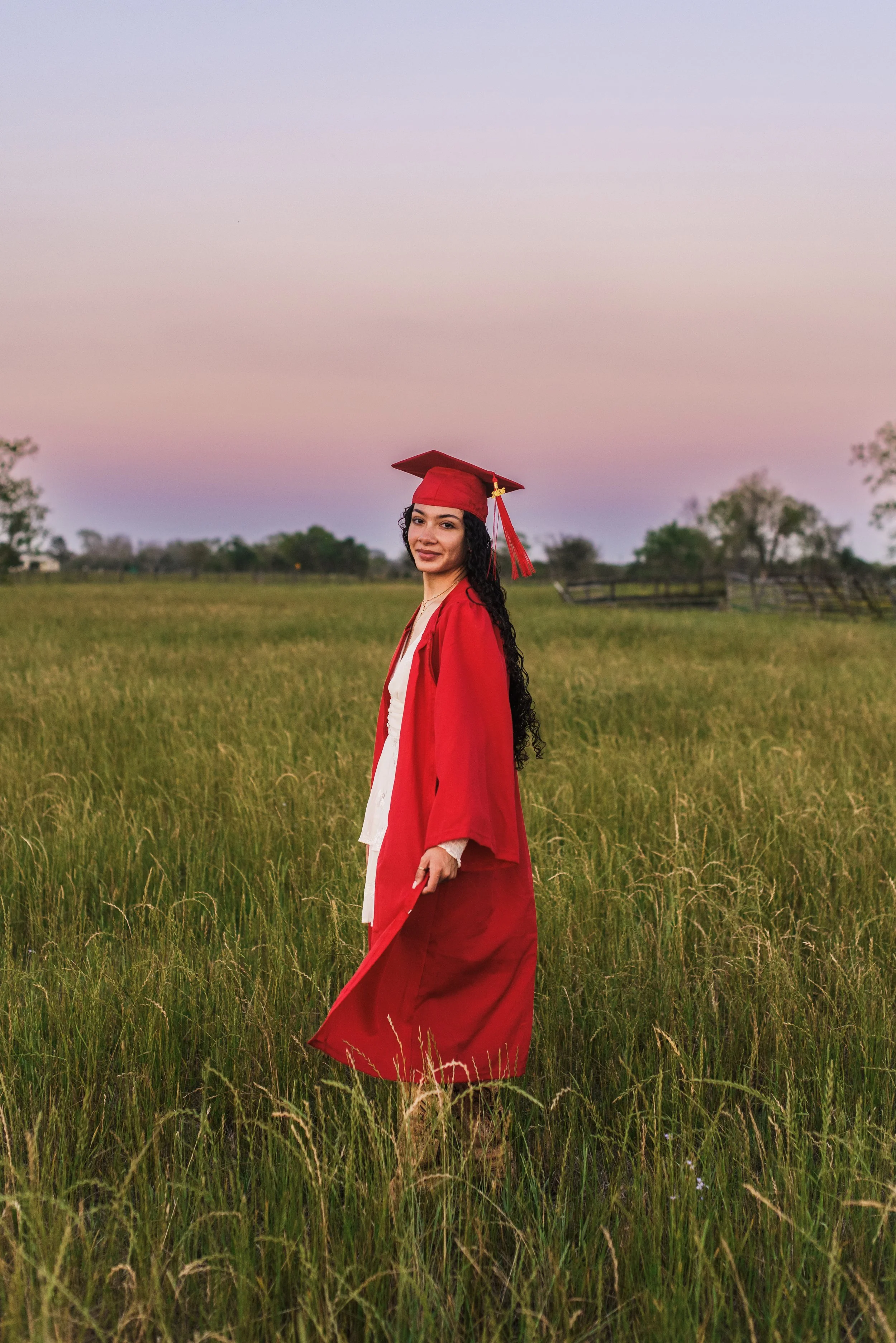 A high school senior girl in her cap and gown in a field 