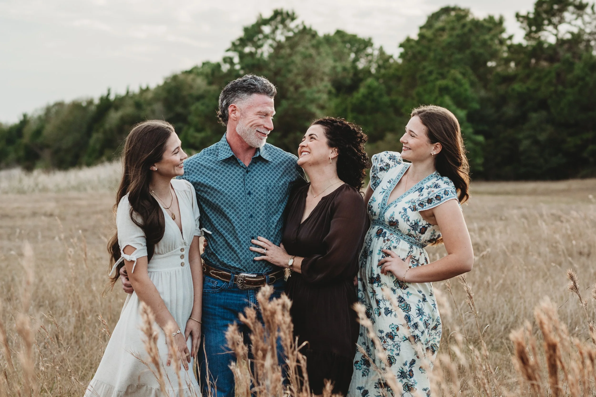 happy connected family with teen girls laughing together while at a photography session in a field