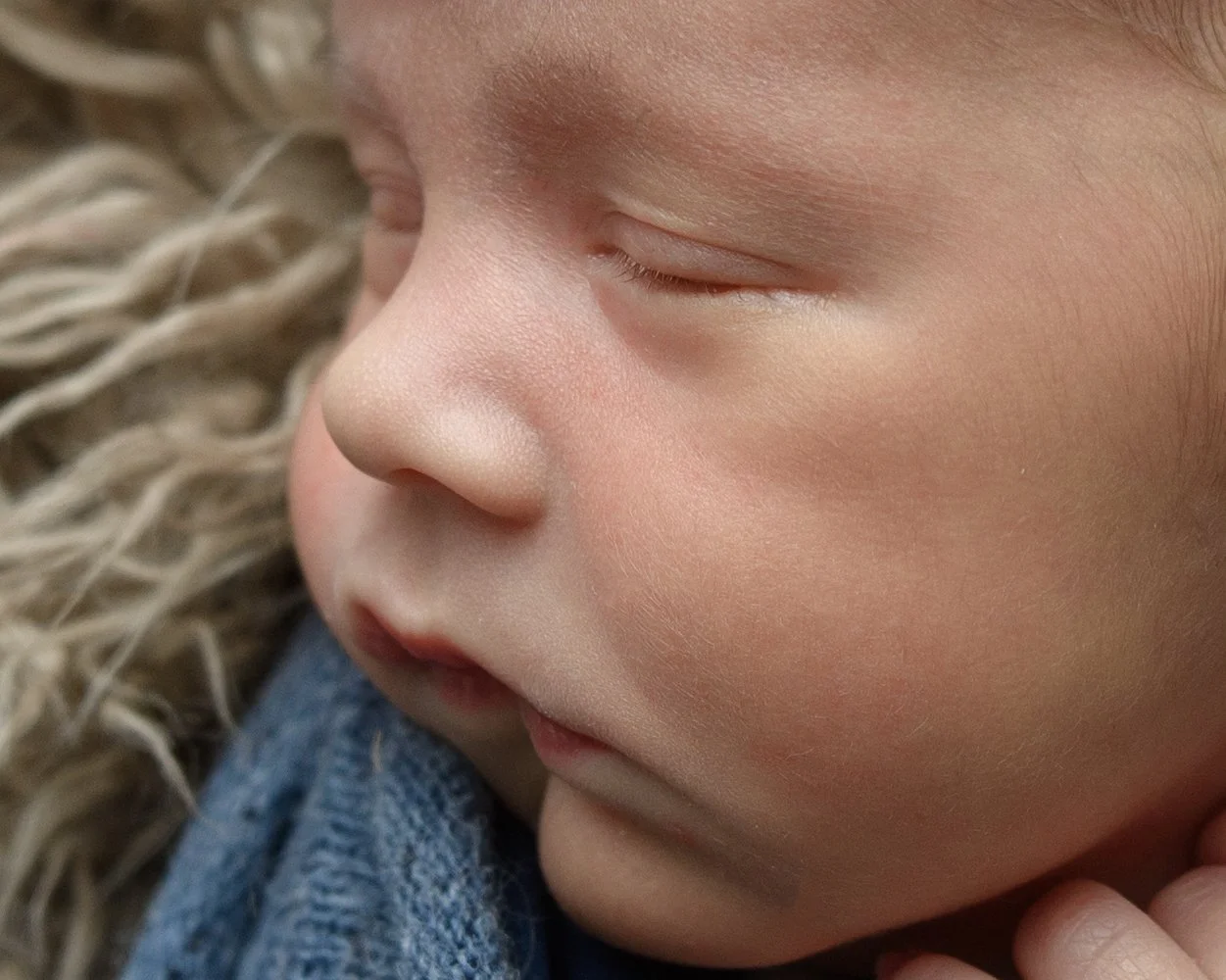 Close-up of a sleeping child's face showing closed eyes, nose, and lips, with curly hair and a blue denim clothing material nearby.