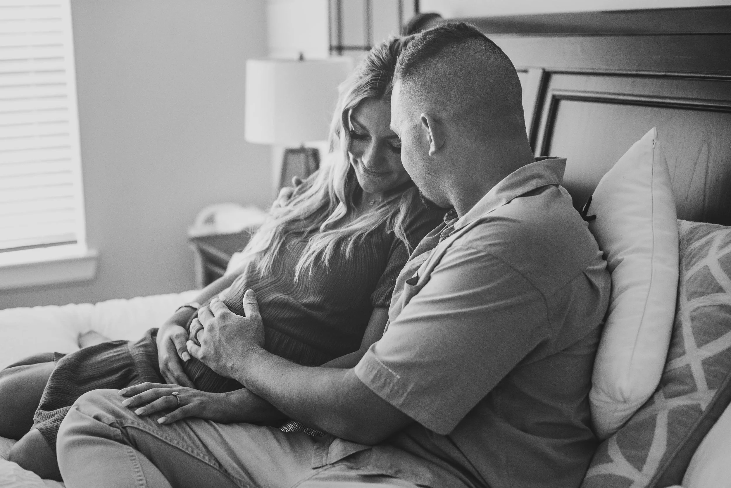 A couple sitting closely on a bed, holding hands, and sharing a tender moment in a bedroom.