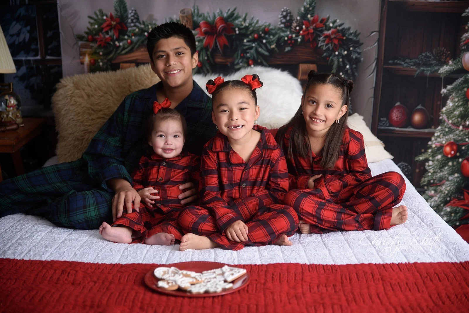 siblings snuggled together with cookies in Christmas pajamas