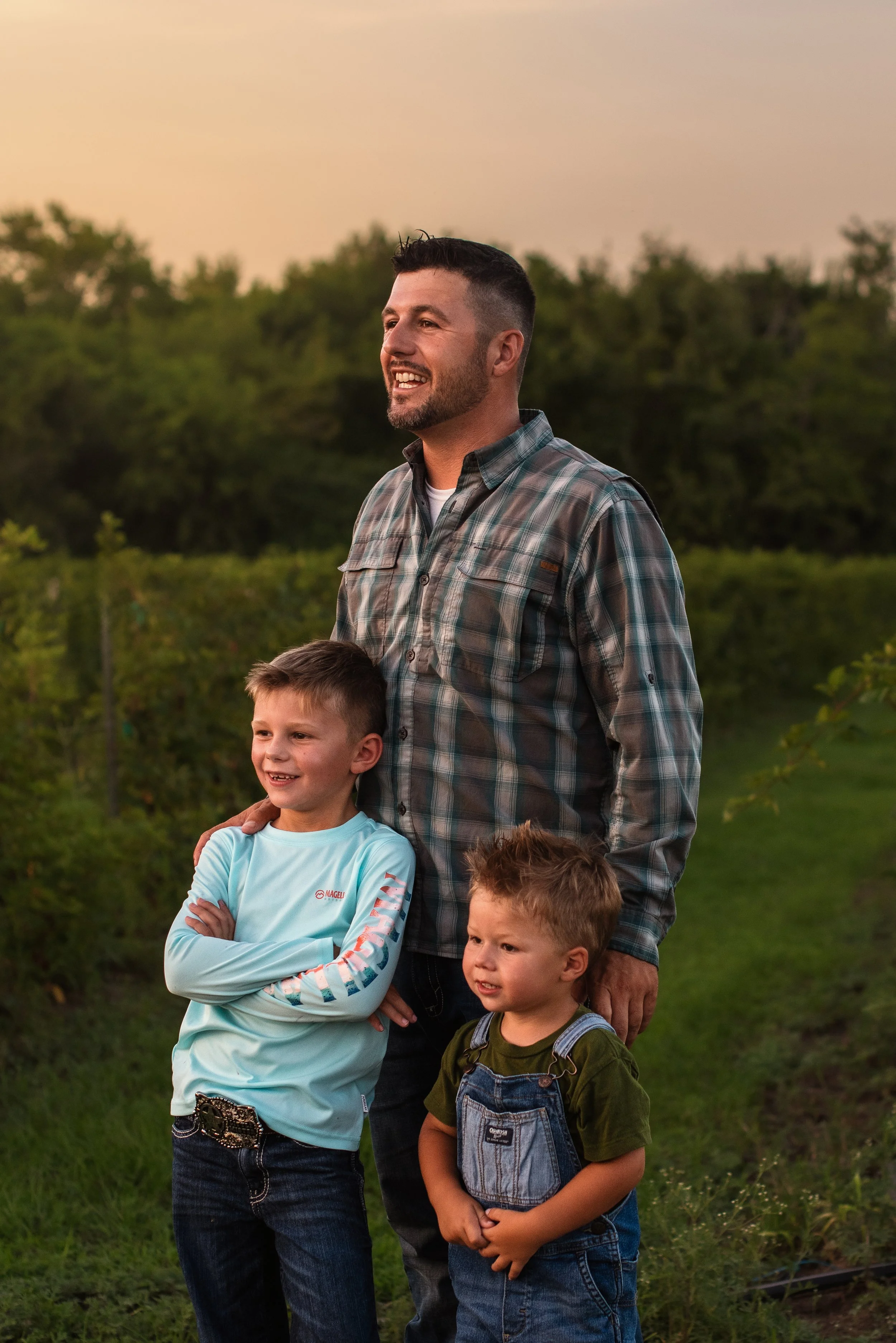A man and three children standing outdoors in a grassy area with trees in the background during sunset.