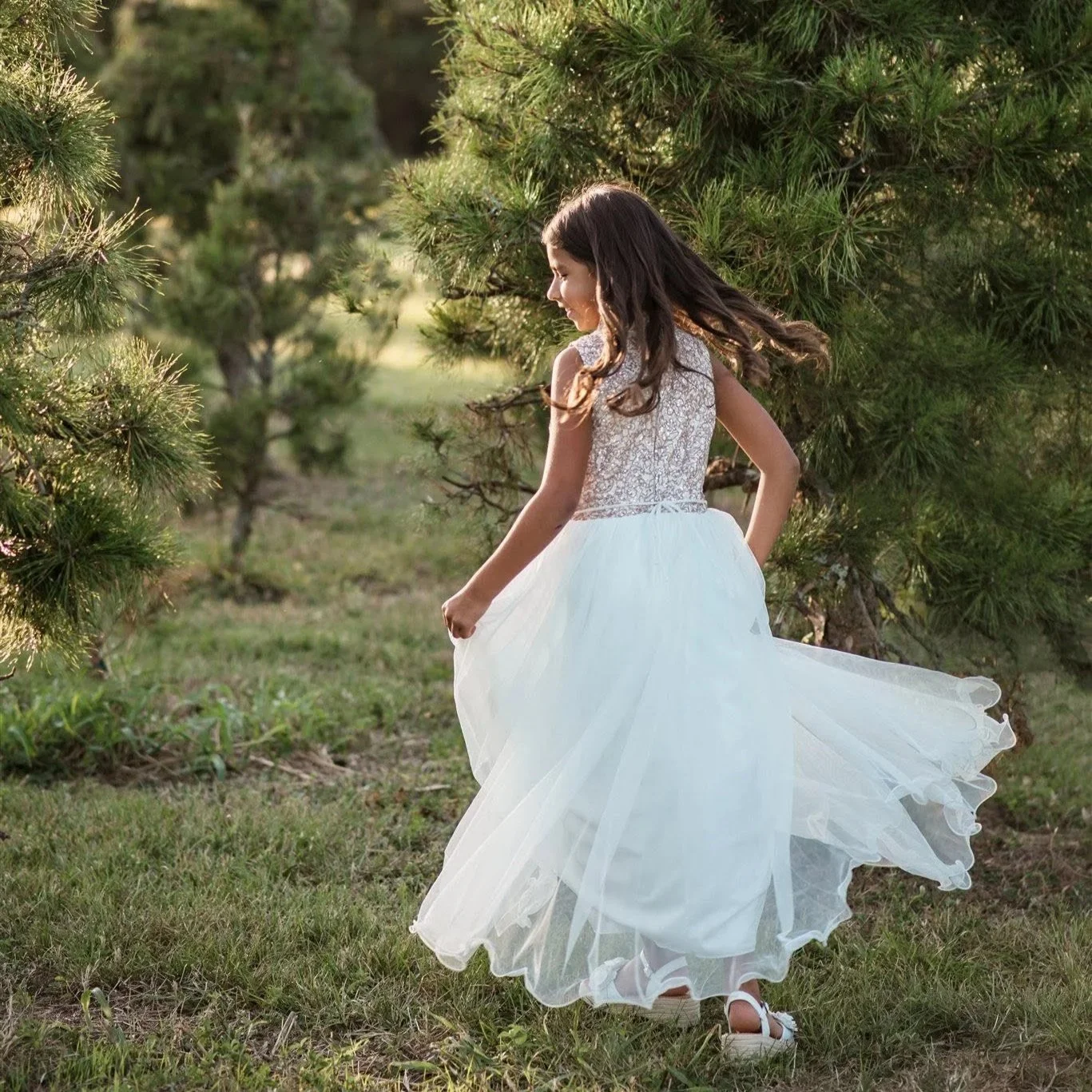 Young girl in a white dress twirling among Christmas trees during a holiday portrait session by Christy White Photography in the Houston area.