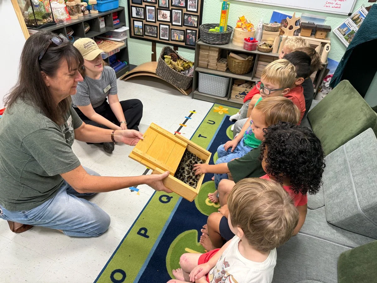 A teacher sitting on the floor with some young students.