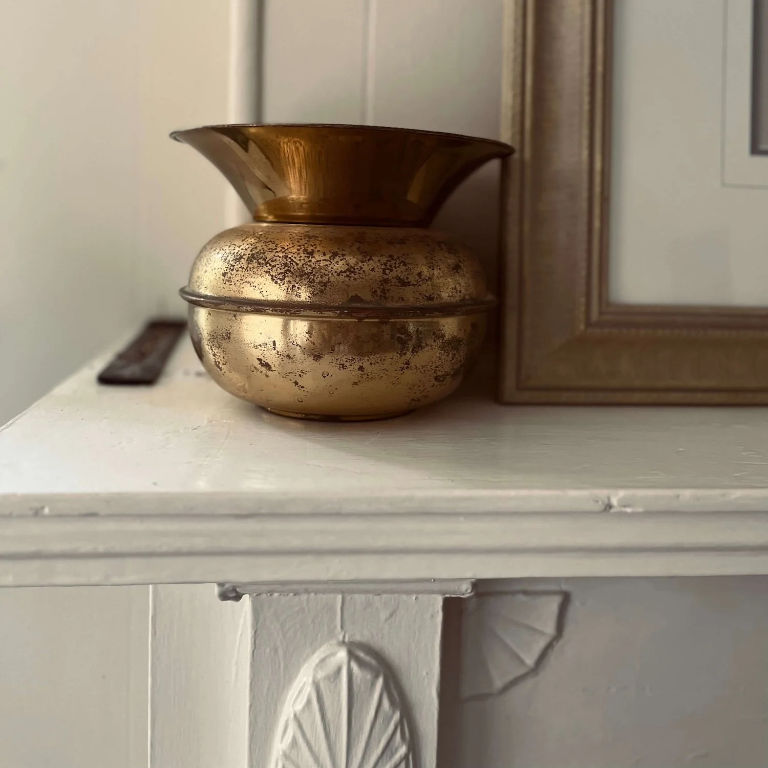 An antique tarnished brass spittoon belonging to the author's paternal great-grandfather, beautifully displayed as a cherished family heirloom on a white mantel in her Greensboro bungalow.