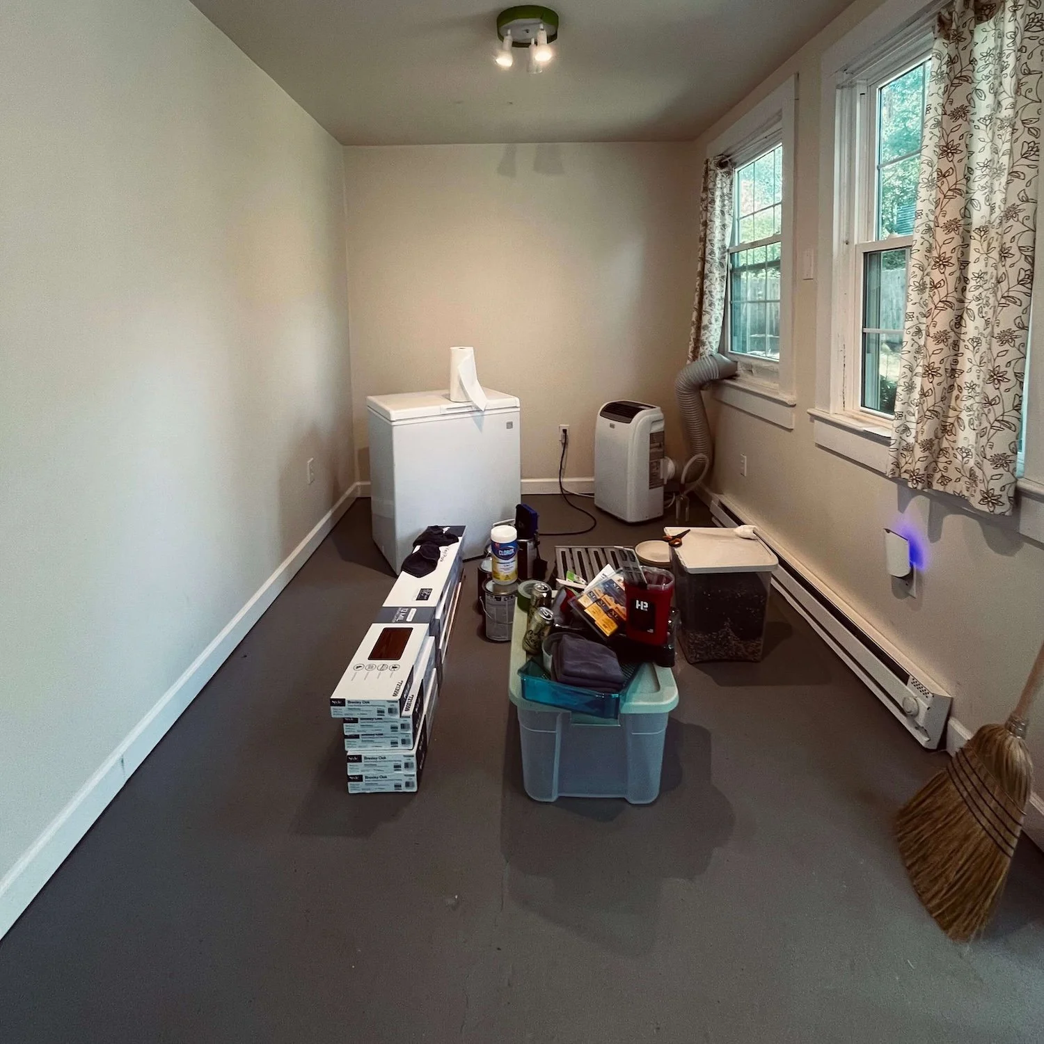 A before picture of the Greensboro backyard apothecary shed interior, showing the small chest freezer, painting supplies, and new flooring materials ready to be installed.