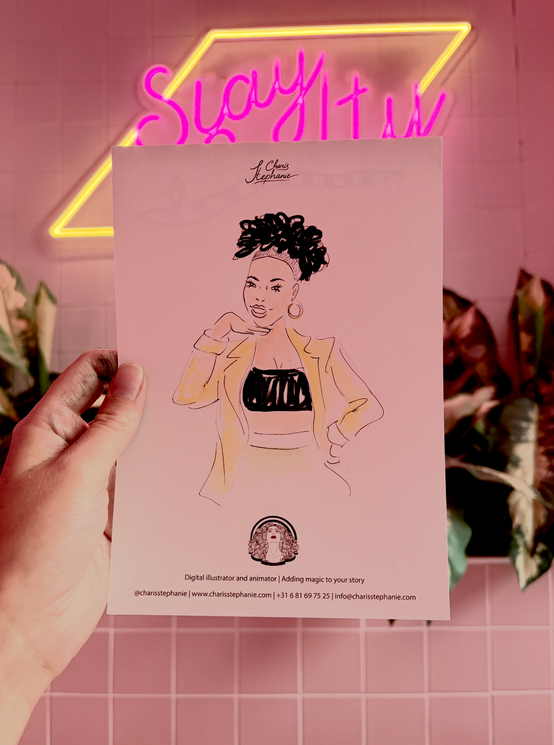 Een hand houdt een illustratie van een vrouw met een afro-knot in haar haar, een gele blazer, een zwart top en grote oorbellen. Op de achtergrond is een neonbord met de tekst 'Stay It' in roze en geel