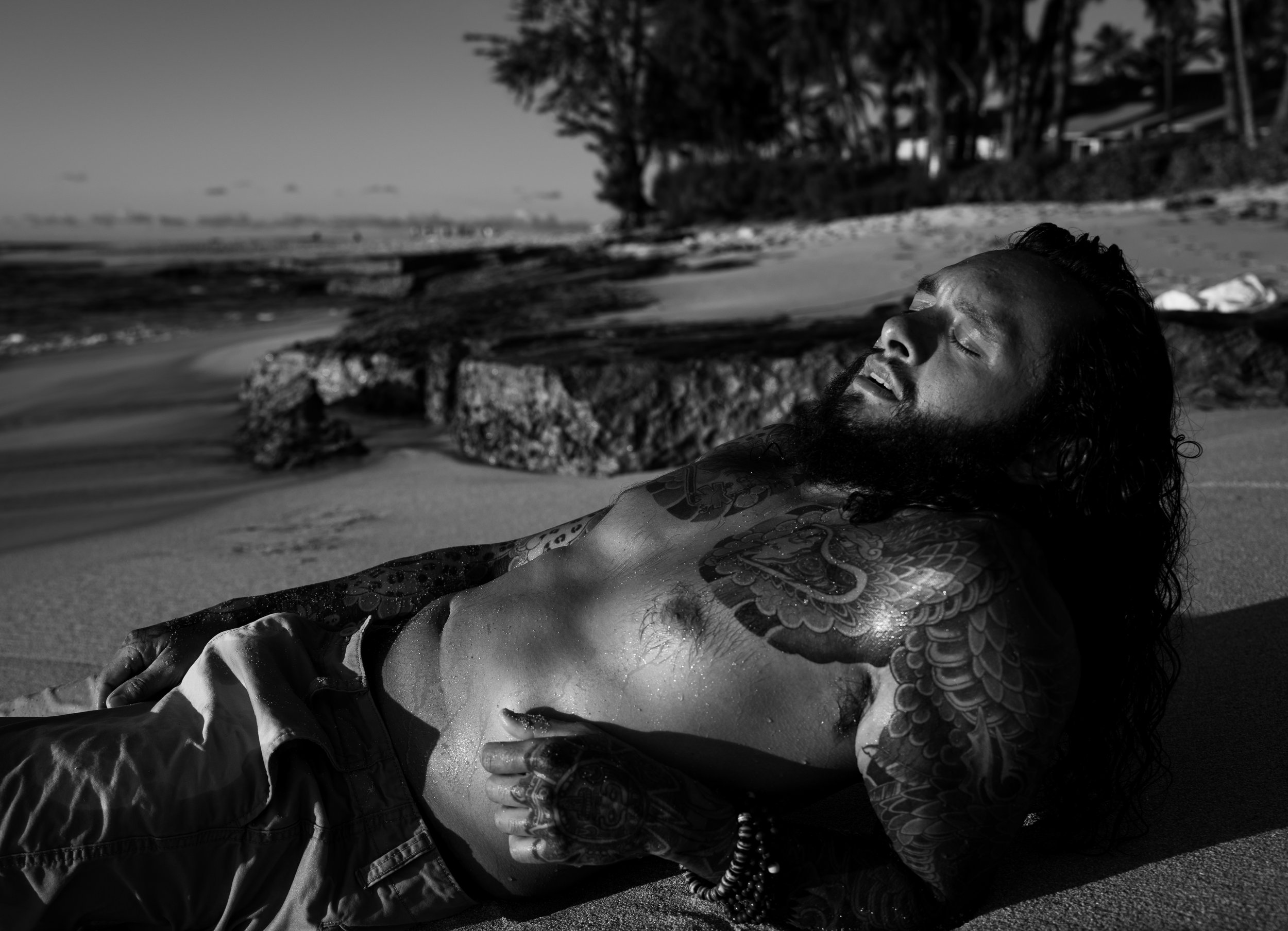 Male laying on a beach of Oahu, Hawaii expressing a sensual exhale during a photoshoot. 