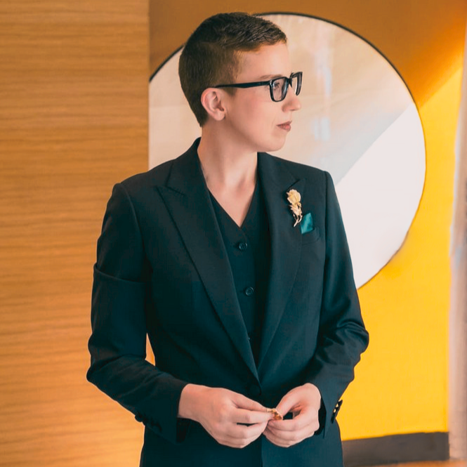 A photo of Ellie Roth in a three-piece suit, looking off into the distance.
