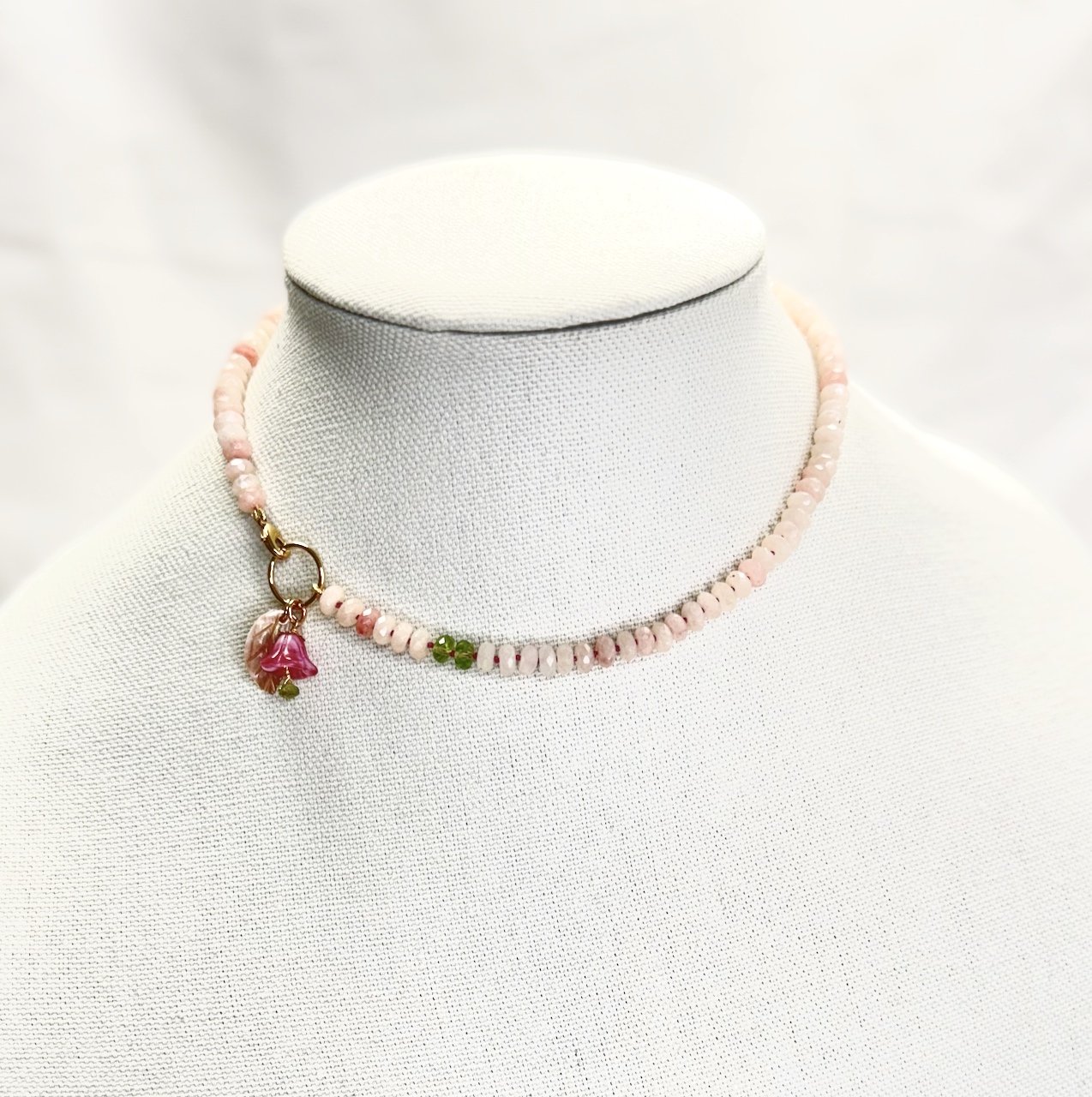 Pale pink magano calcite necklace knotted with pink thread, featuring peridot accents, glass flower and shell leaf charms, and a gold filled lobster clasp.