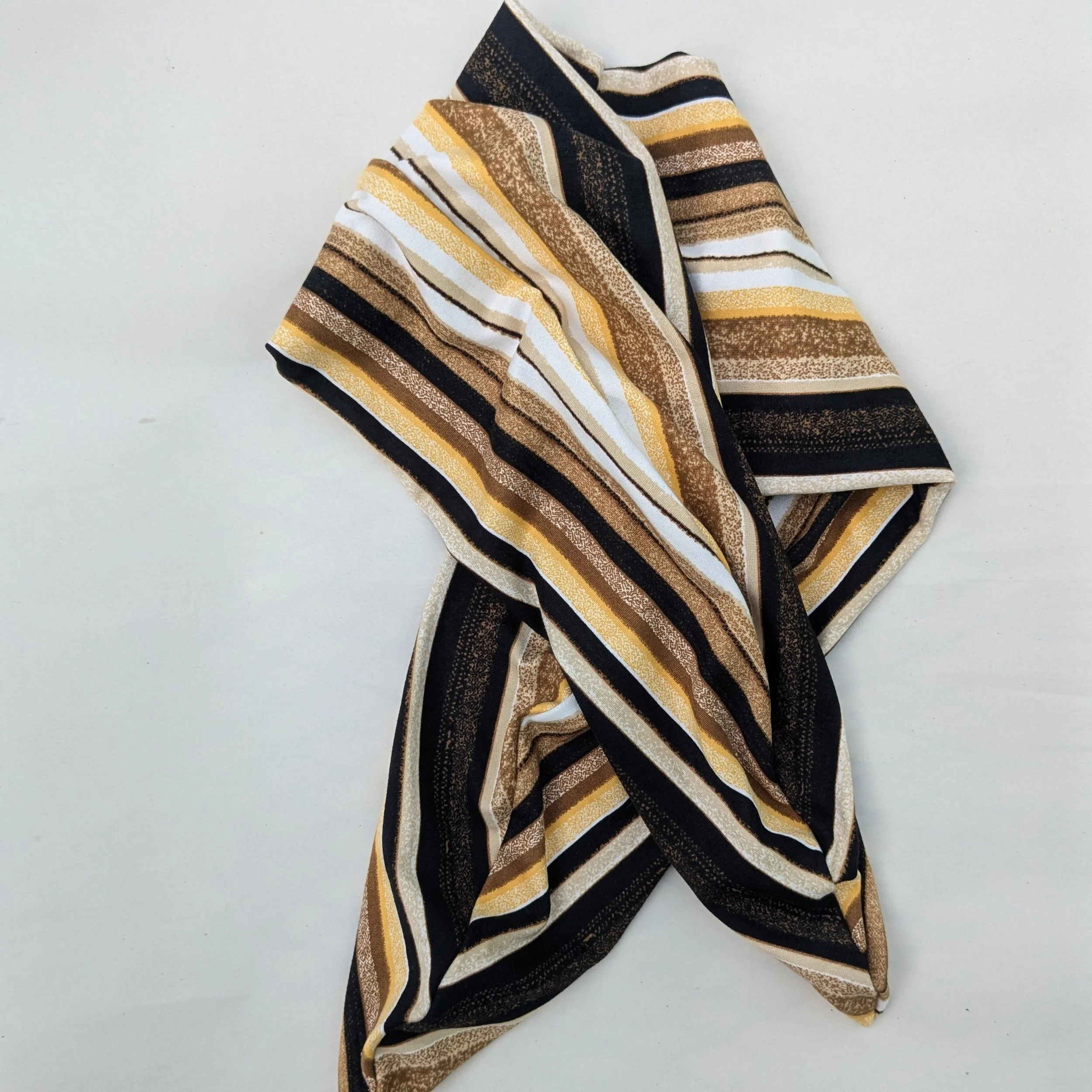A multi-colored yellow, brown, black and white striped knit headband placed loose on the table