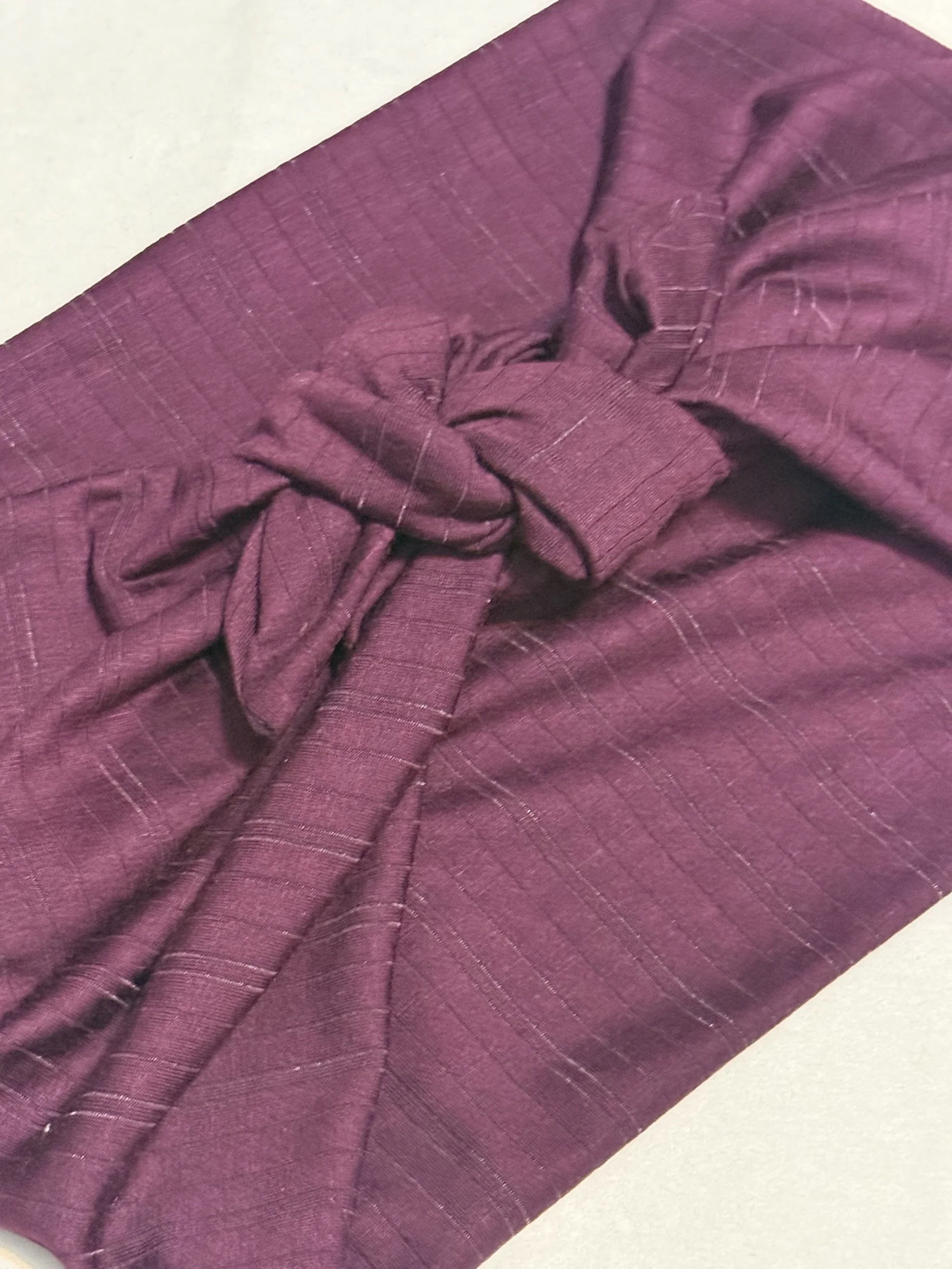 A plum purple with plum purple striped headband tide in a square knot