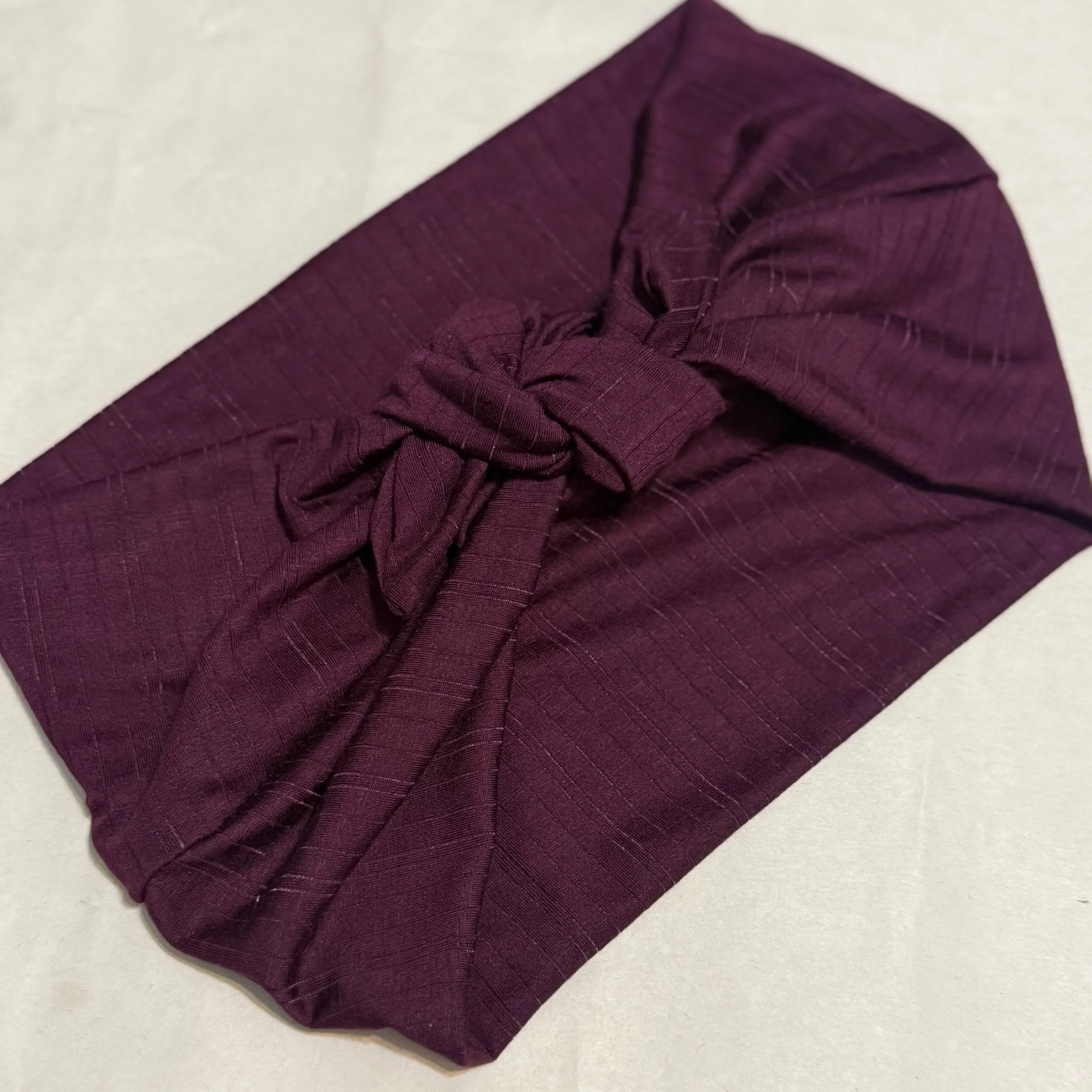 A plum purple with plum purple striped headband tide in a square knot