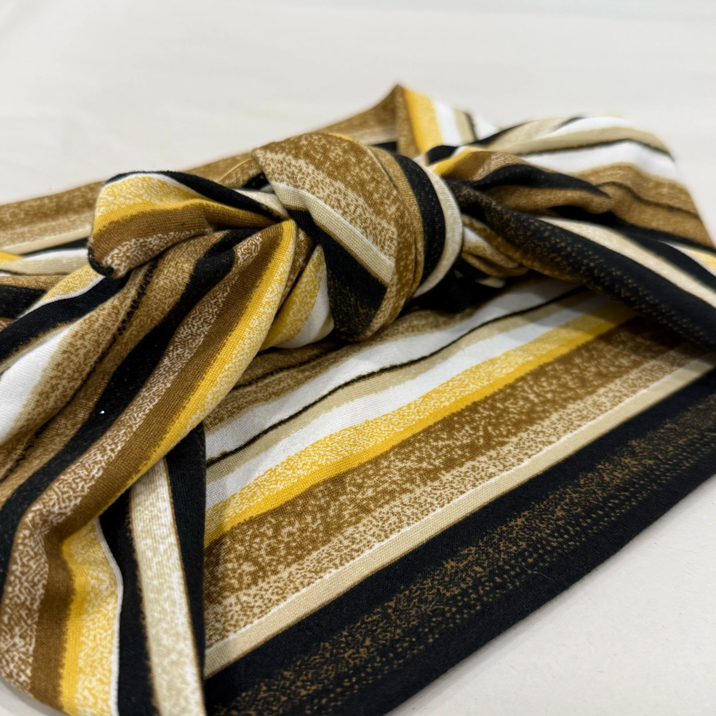 A multi-colored yellow, brown, black and white striped knit headband tide in a square knot