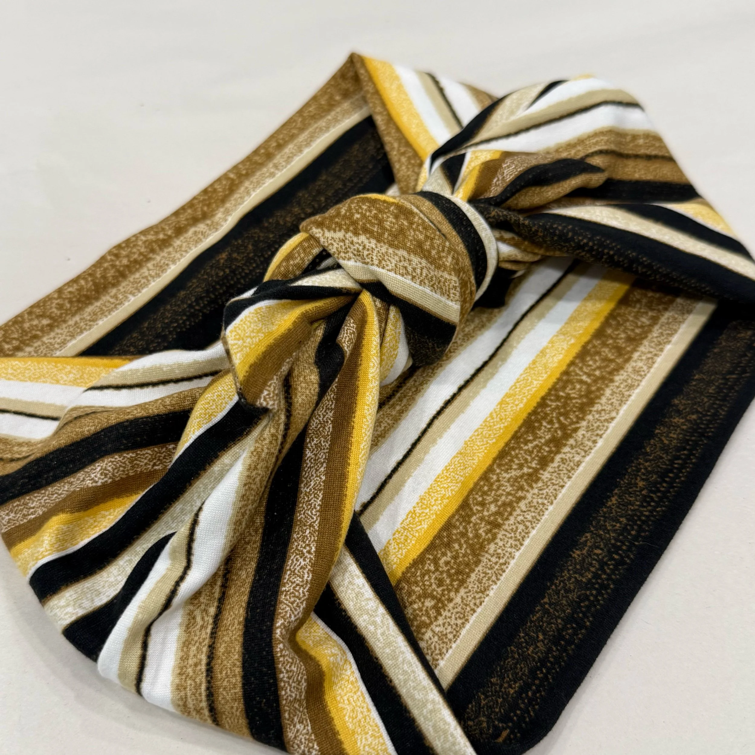 A multi-colored yellow, brown, black and white striped knit headband tide in a square knot