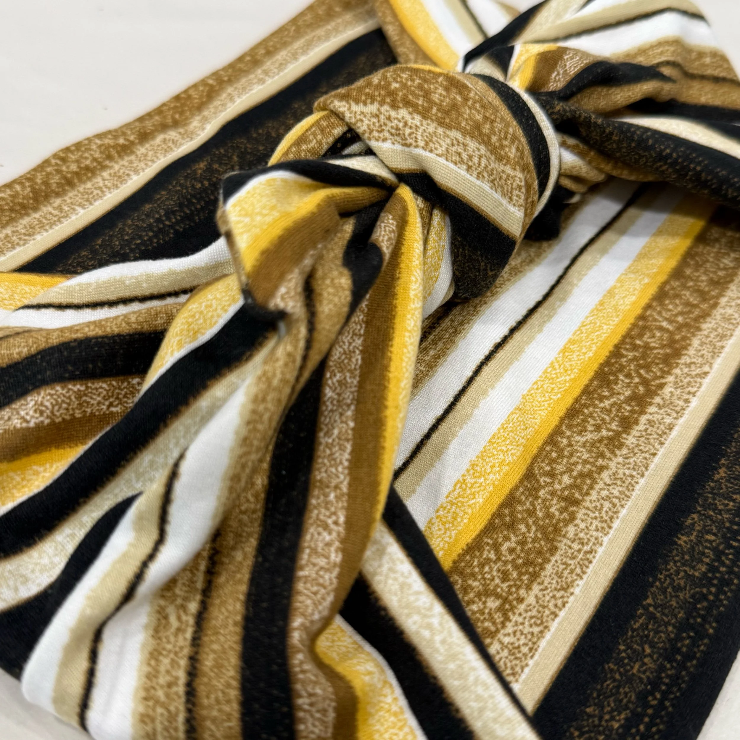 A multi-colored yellow, brown, black and white striped knit headband tide in a square knot