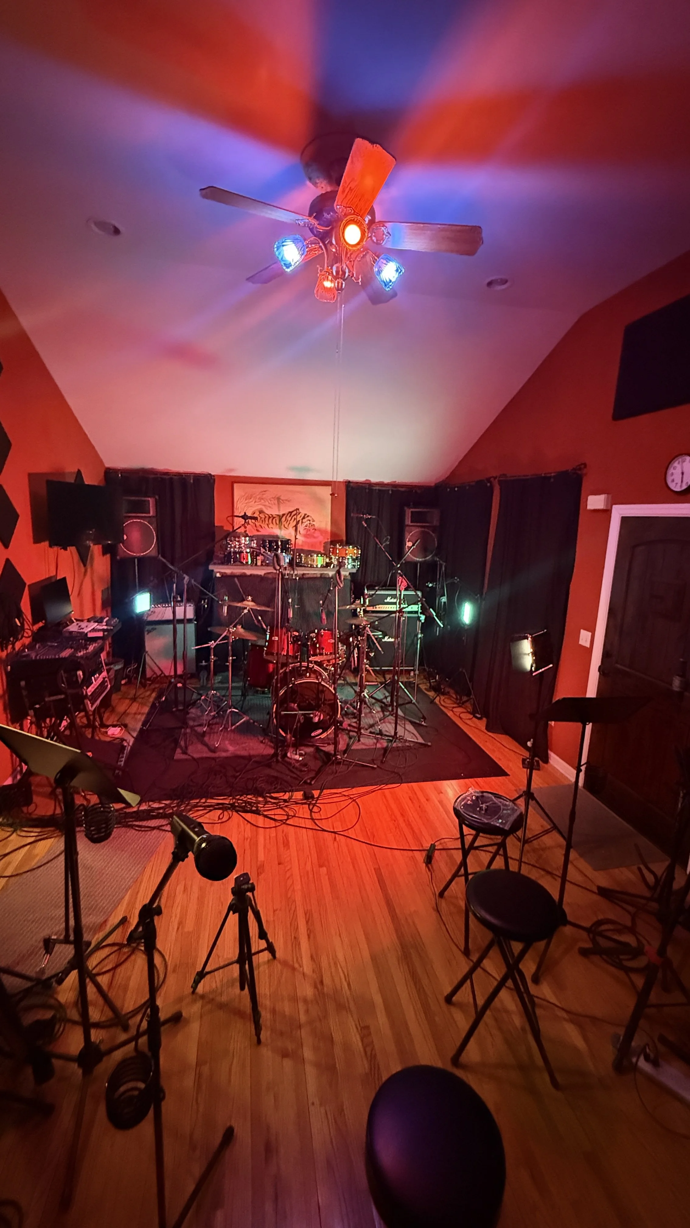 Music recording studio with a drum set, microphones, chairs, and colored lighting, ready for a performance or recording session.